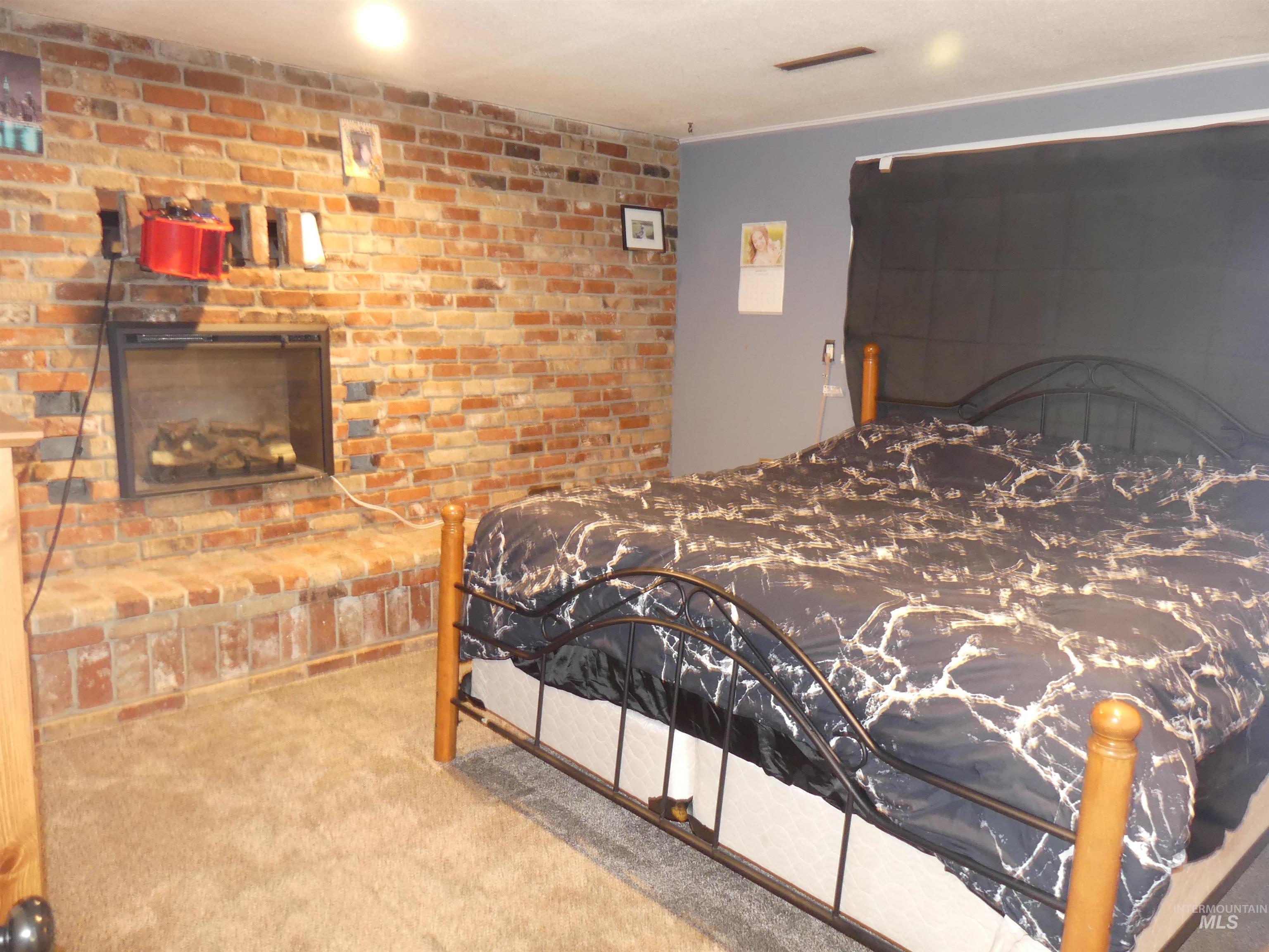Bedroom featuring a fireplace, carpet flooring, and brick wall