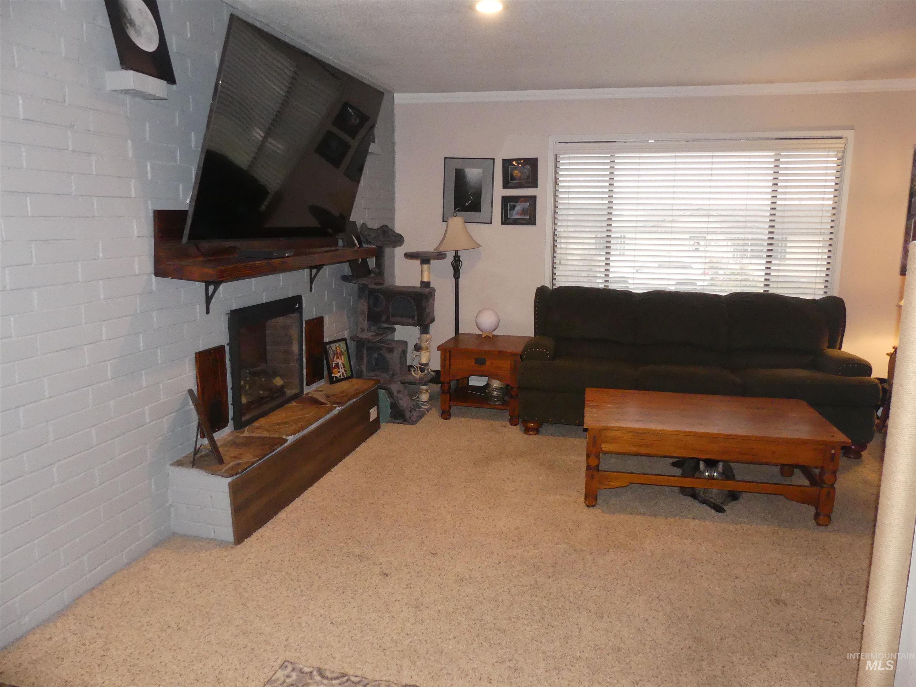 Carpeted living room featuring a fireplace, crown molding, and brick wall