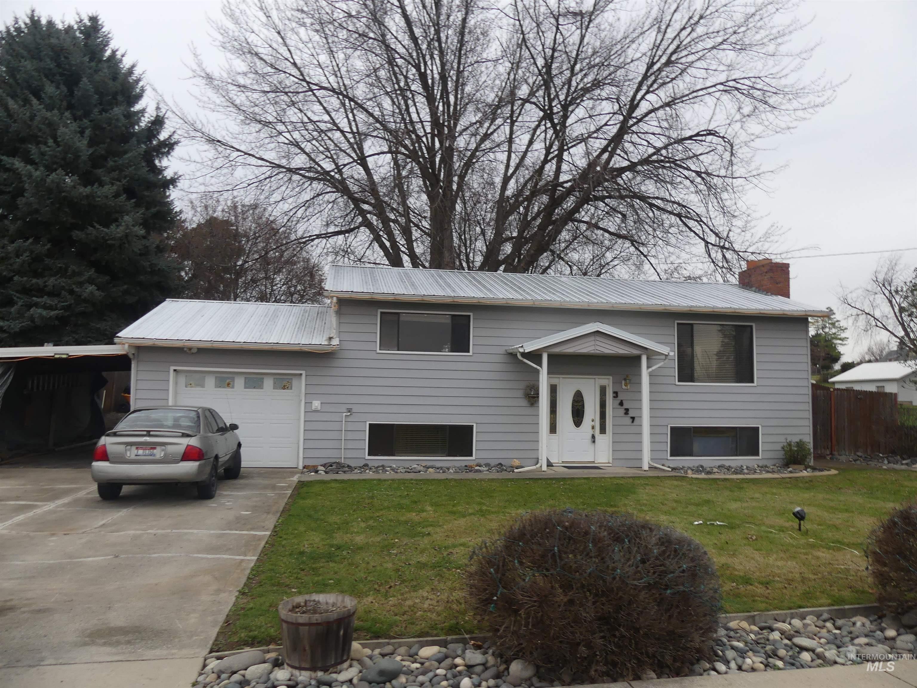Raised ranch featuring concrete driveway, a chimney, an attached garage, a metal roof, and a carport