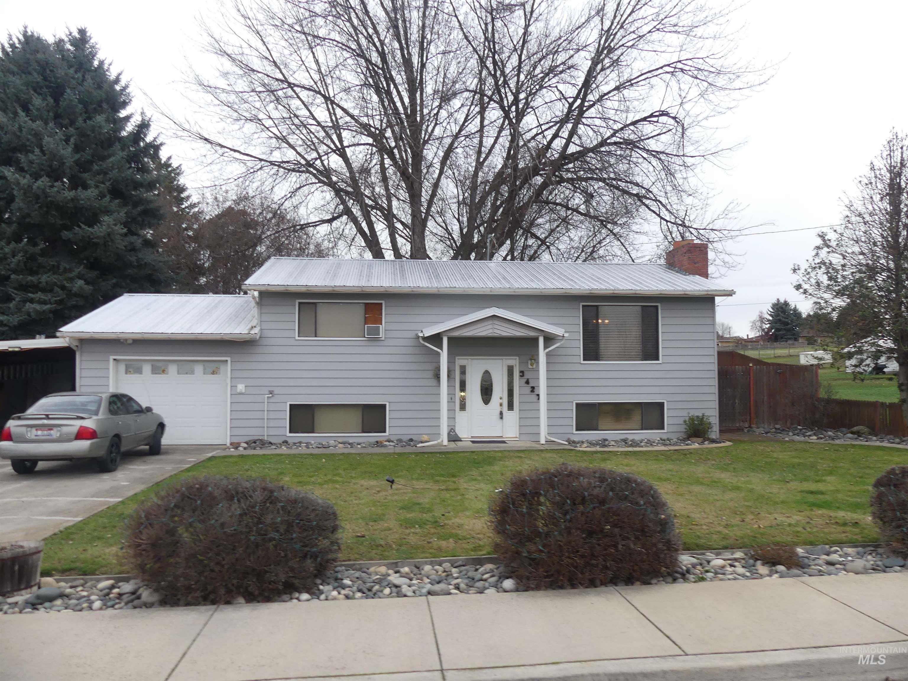 Raised ranch with driveway, a chimney, a garage, and a metal roof