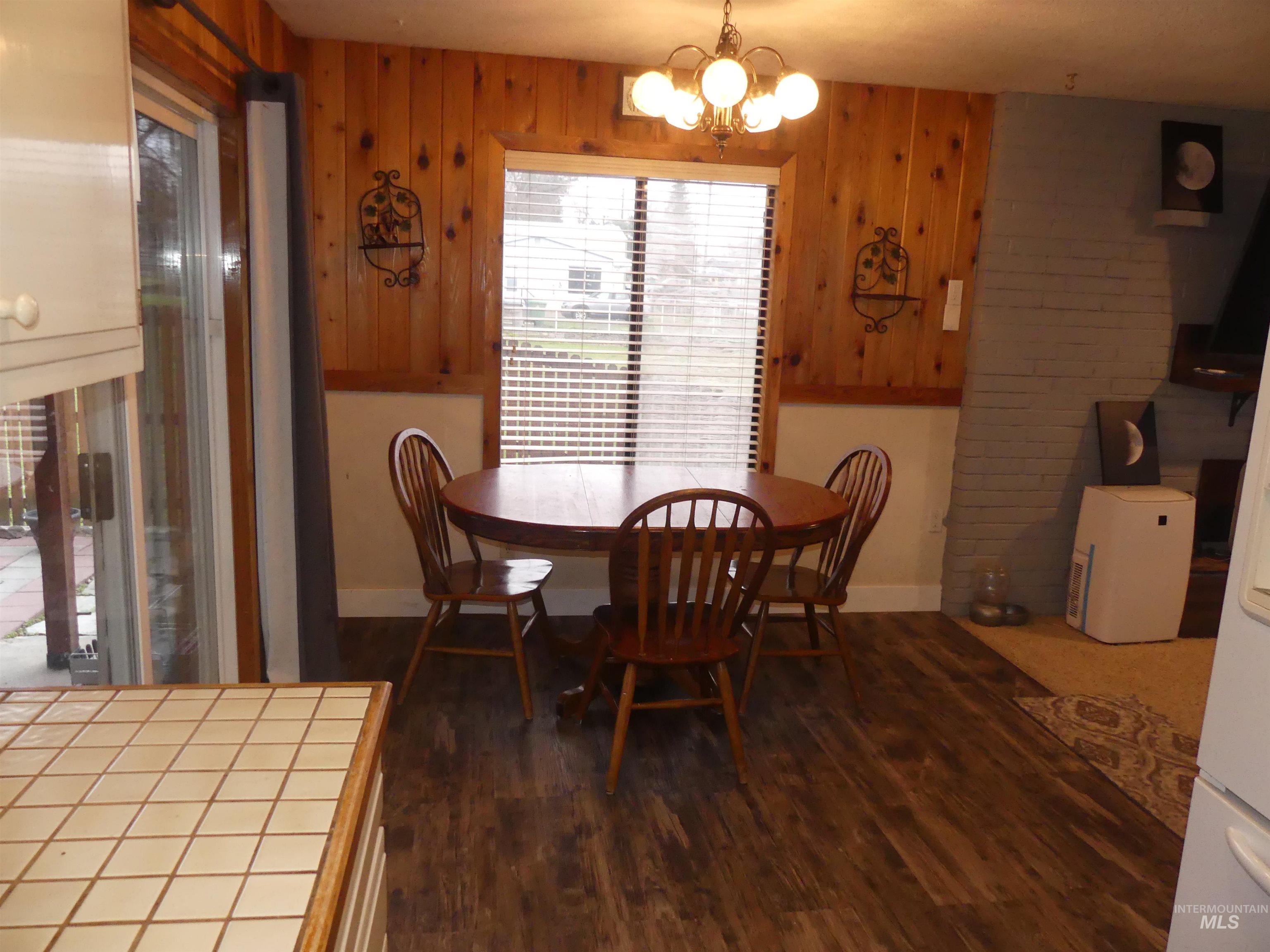 Dining area with dark wood-type flooring, a chandelier, and wooden walls