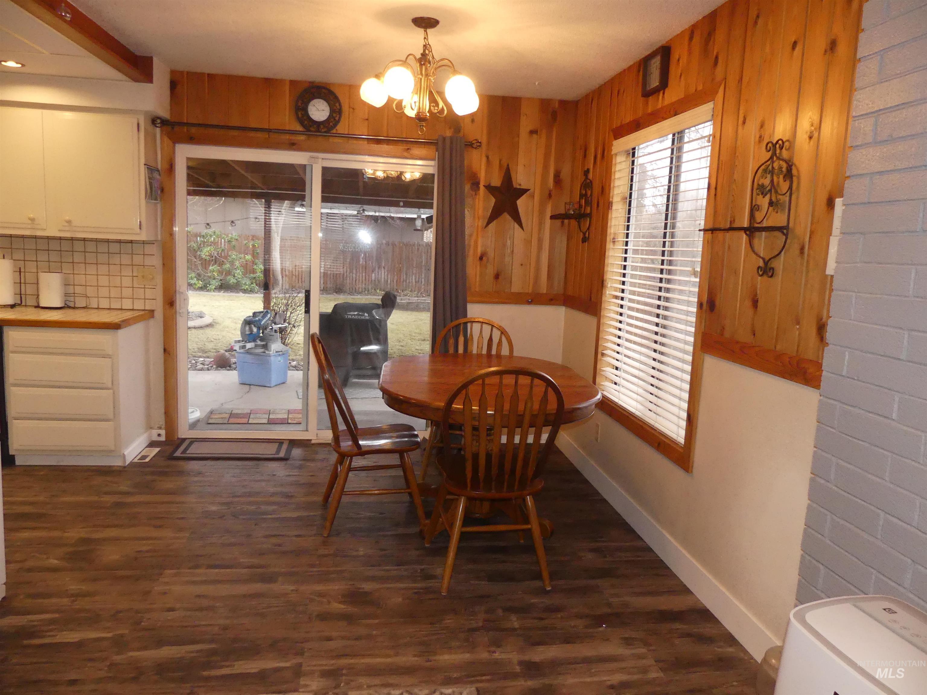 Dining area with dark wood finished floors, a chandelier, and wood walls