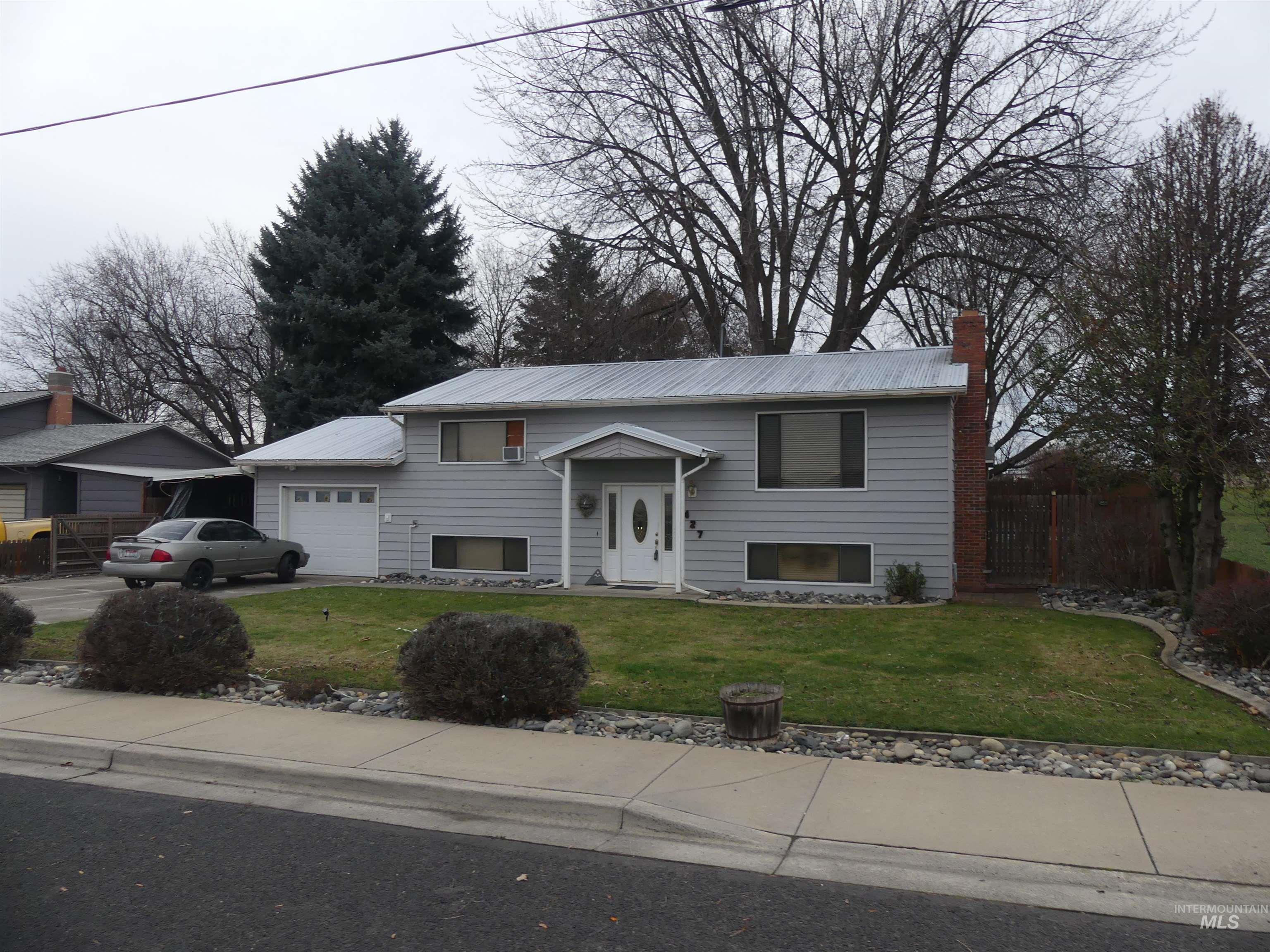 Split foyer home featuring a chimney, an attached garage, driveway, and a metal roof