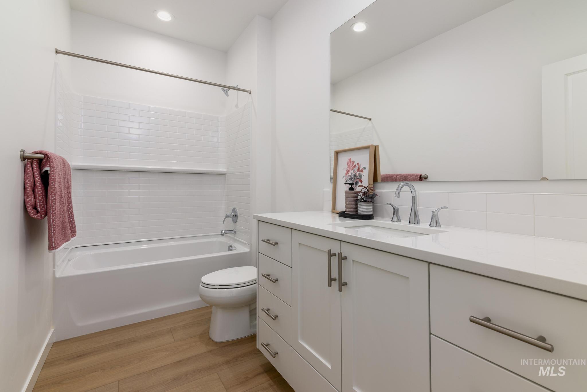 Full bath with light wood finished floors, shower / washtub combination, vanity, and recessed lighting