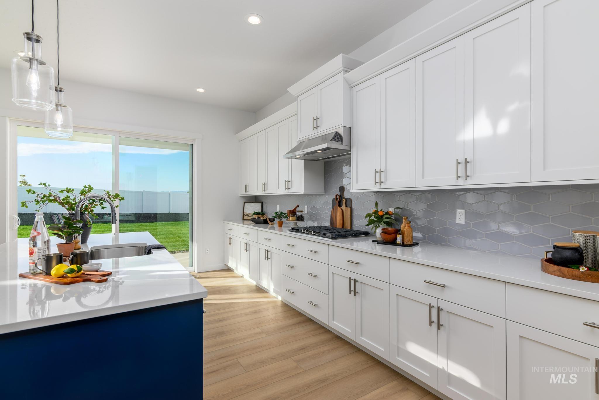 Kitchen with pendant lighting, white cabinets, light wood-style flooring, tasteful backsplash, and light stone counters