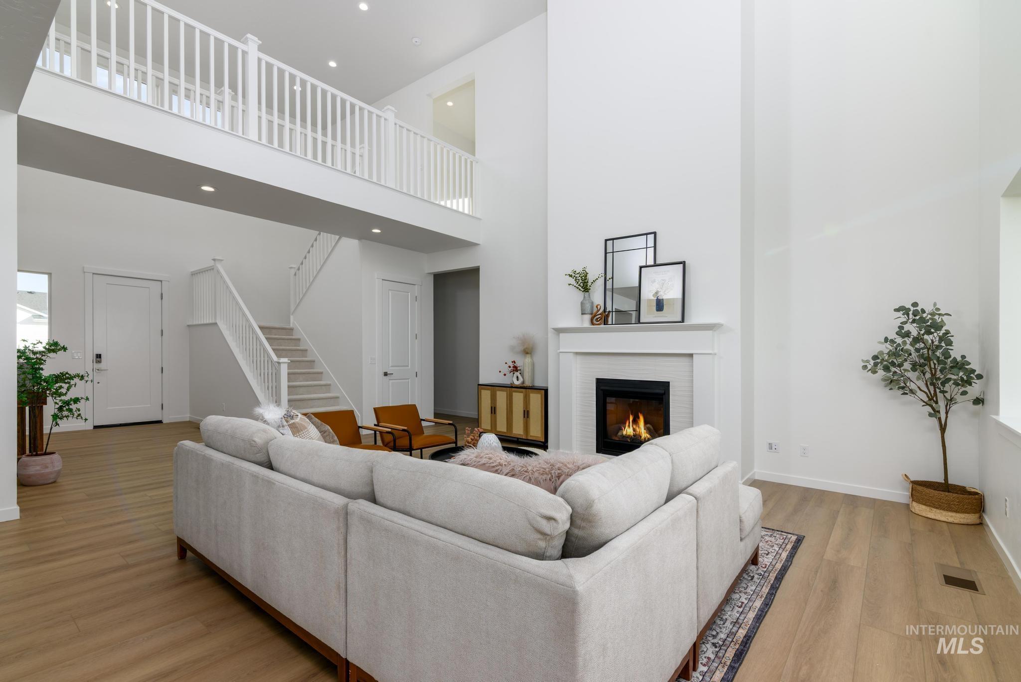 Living room with light wood-style floors, a fireplace, stairs, a towering ceiling, and recessed lighting