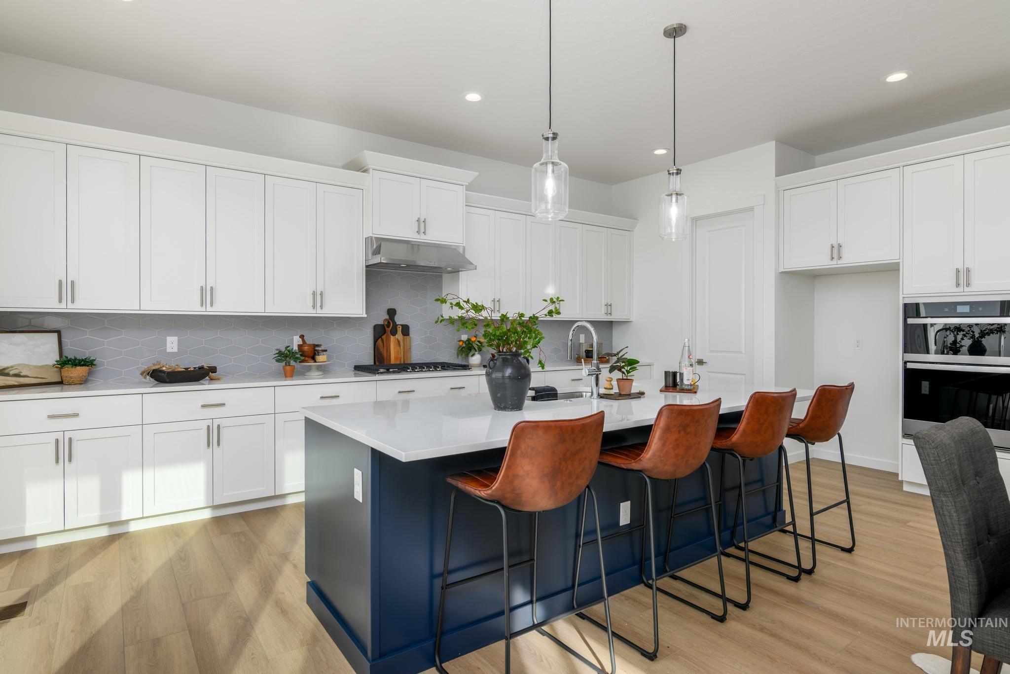 Kitchen featuring a kitchen island with sink, tasteful backsplash, light wood finished floors, a breakfast bar area, and recessed lighting
