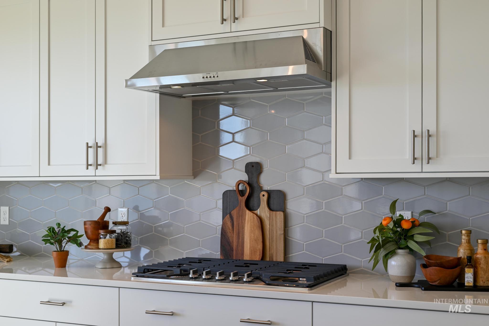 Kitchen featuring white cabinetry, under cabinet range hood, backsplash, and light stone counters