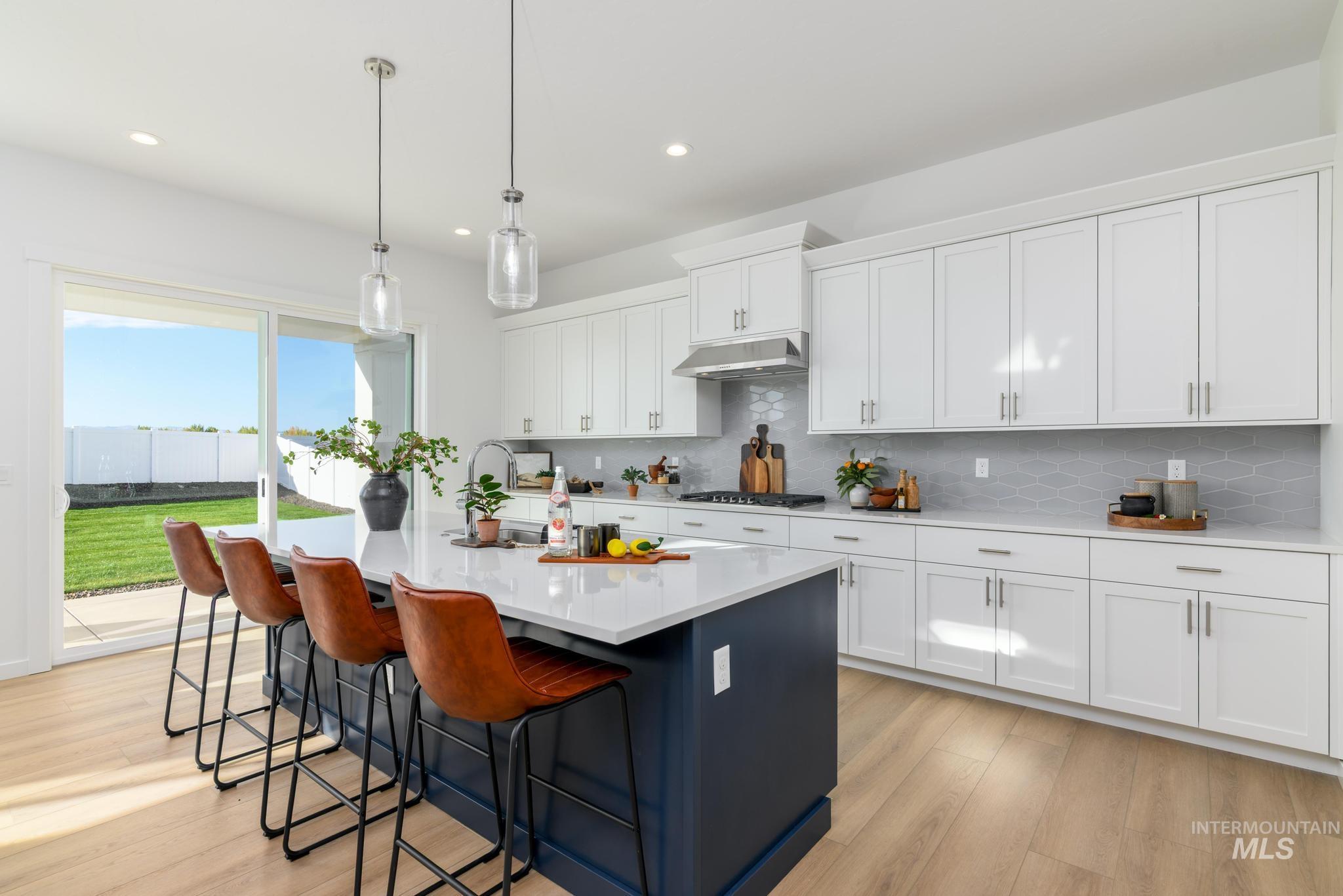 Kitchen with white cabinets, backsplash, an island with sink, light wood-style flooring, and decorative light fixtures