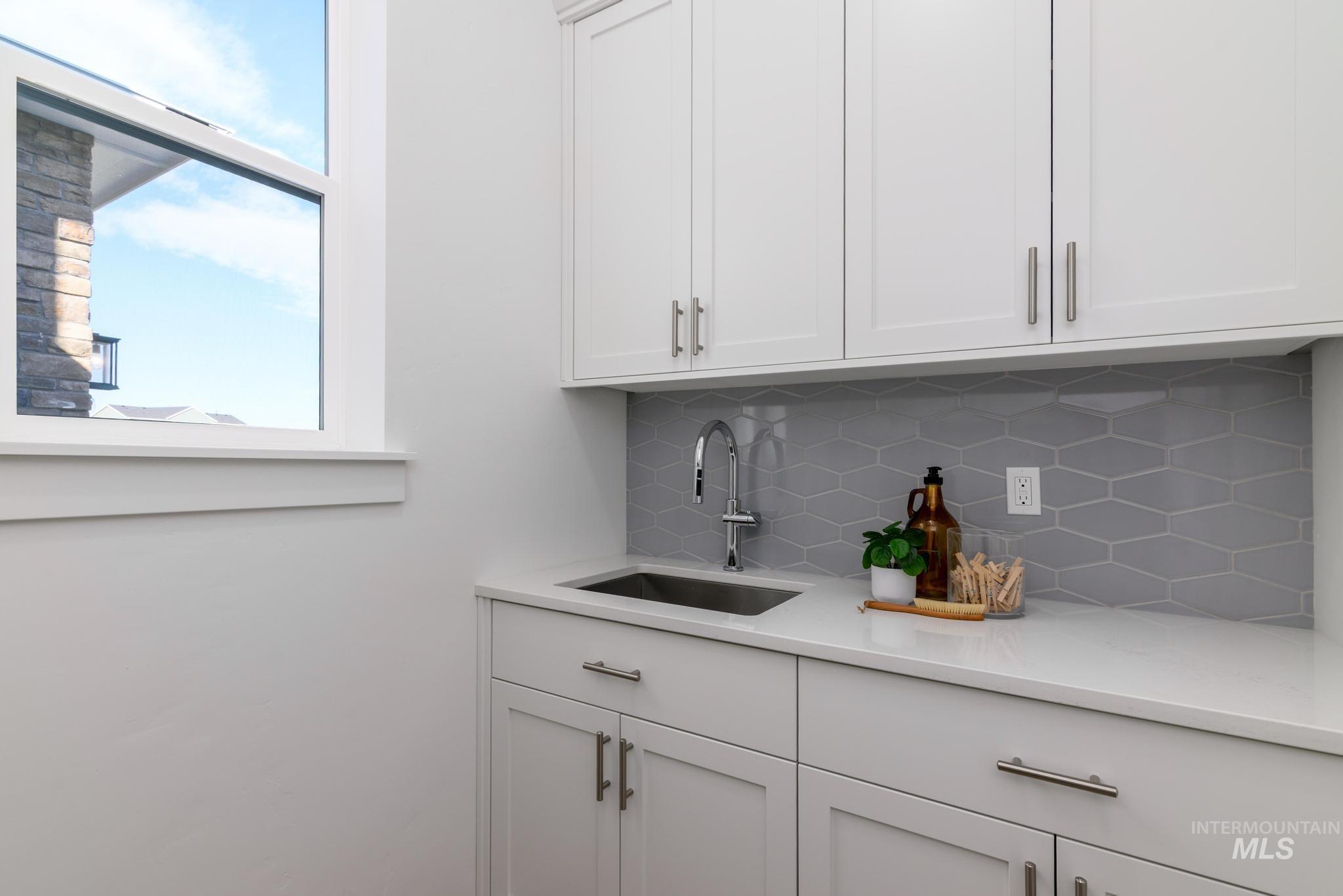 Indoor wet bar featuring backsplash, white cabinetry, and light stone counters