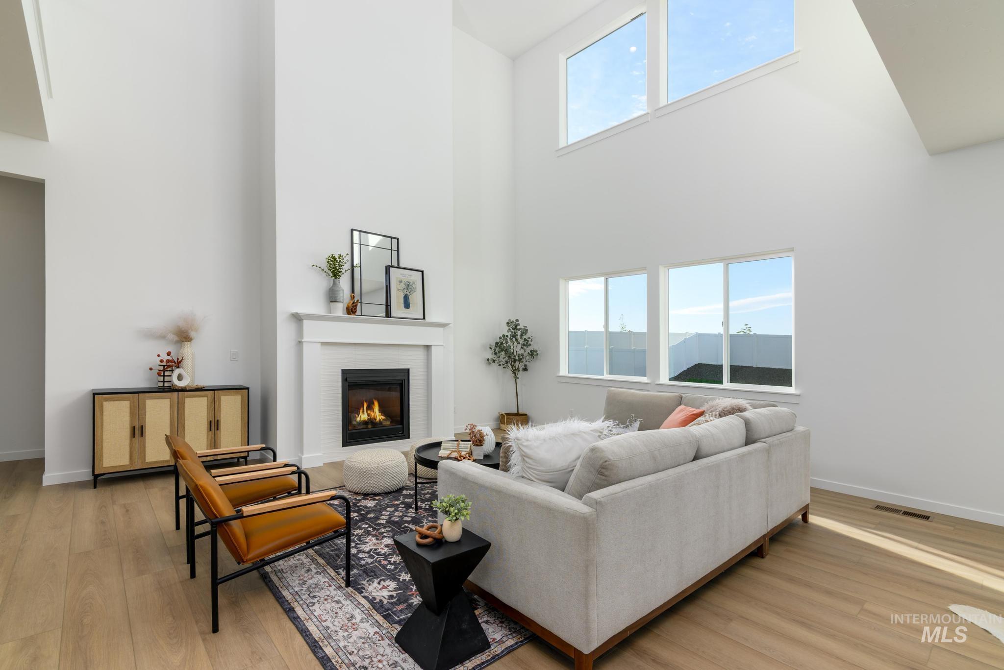 Living area featuring plenty of natural light, a brick fireplace, light wood-style floors, and a high ceiling