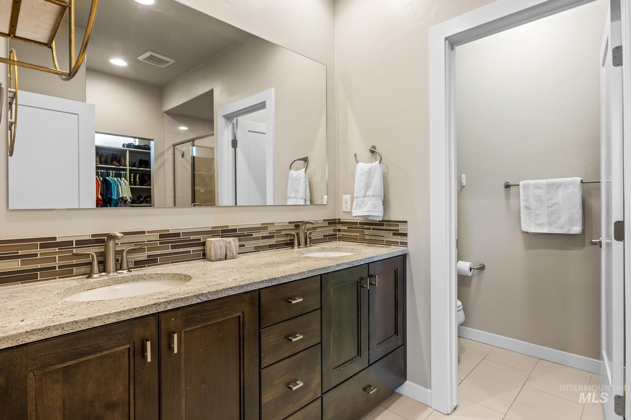 Full bath with a spacious closet, tasteful backsplash, double vanity, a stall shower, and light tile patterned flooring