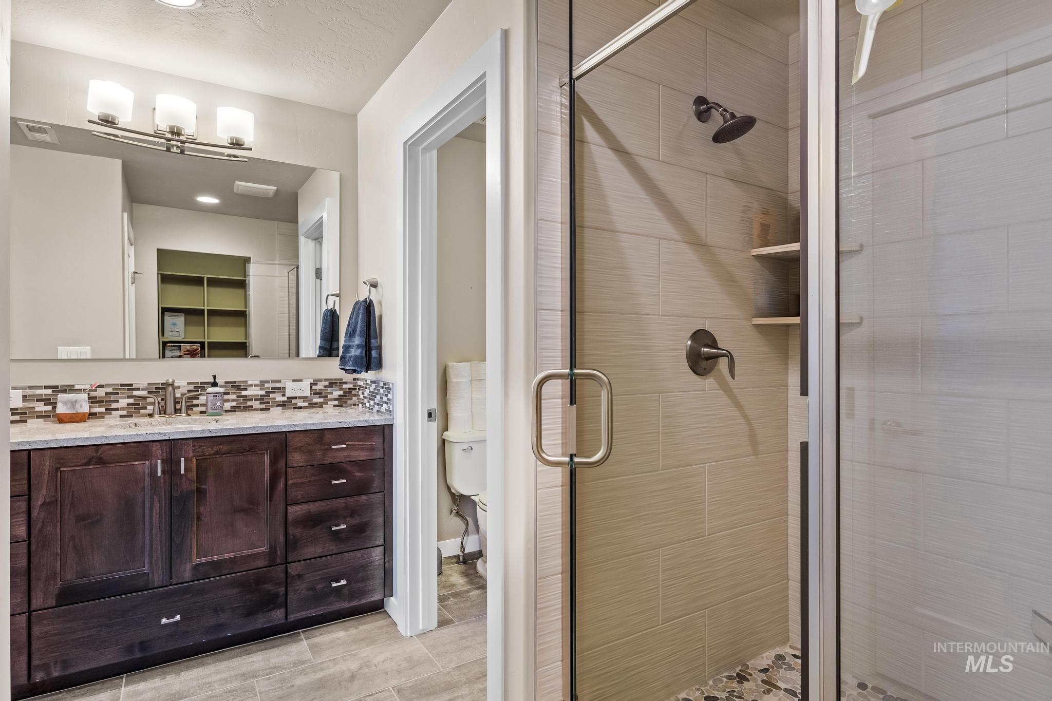 Full bath with a shower stall, vanity, decorative backsplash, a walk in closet, and a textured ceiling