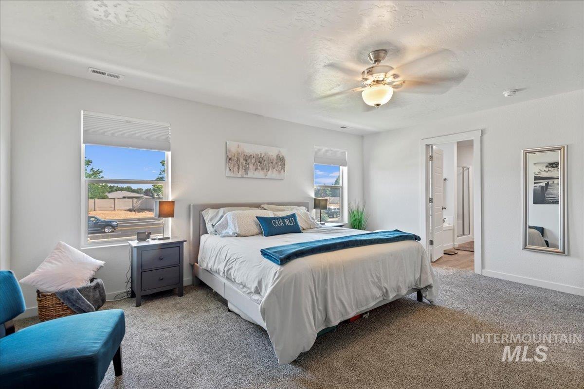 Bedroom with light carpet, a textured ceiling, ceiling fan, and ensuite bathroom