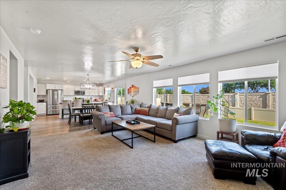 Living room featuring a textured ceiling, light colored carpet, ceiling fan, and a chandelier