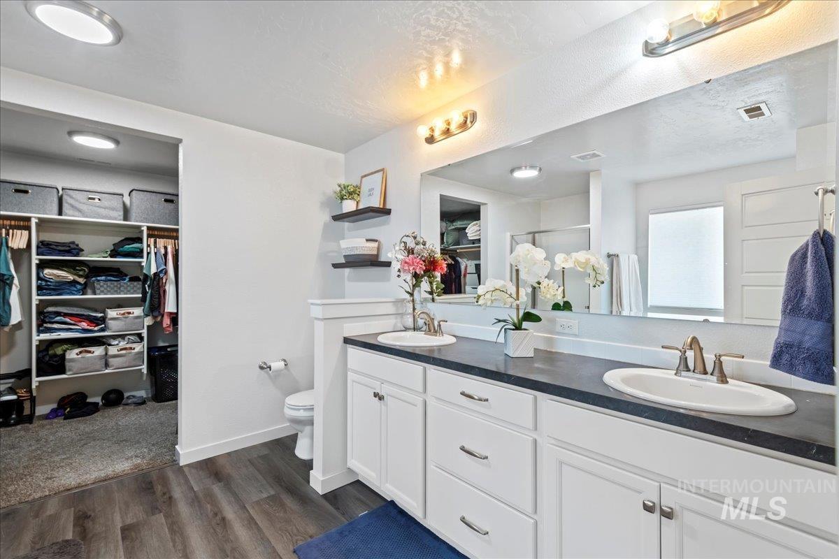 Full bath featuring a spacious closet, double vanity, engineered vinyl plank-type flooring, a stall shower, and a textured ceiling