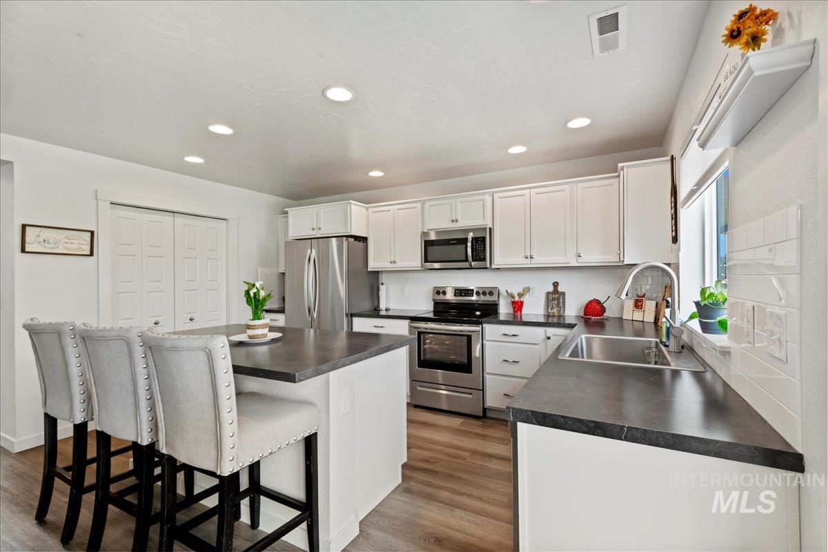 Kitchen featuring dark countertops, appliances with stainless steel finishes, white cabinetry, engineered vinyl plank-type flooring, and a center island