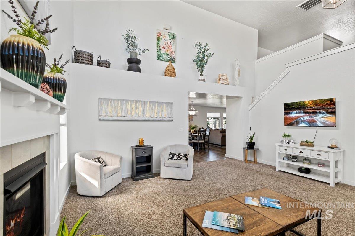 Carpeted living room featuring a tiled fireplace and a high ceiling
