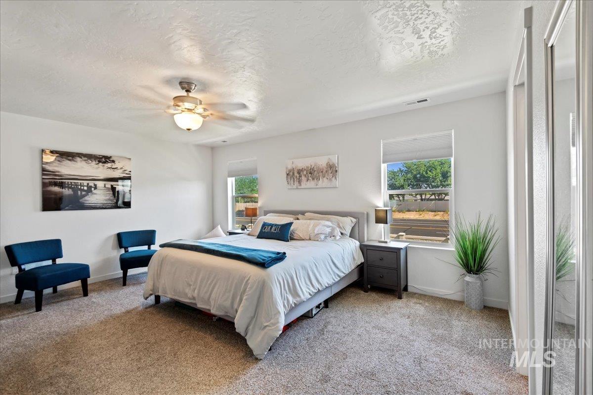 Bedroom featuring light carpet, multiple windows, a textured ceiling, and ceiling fan