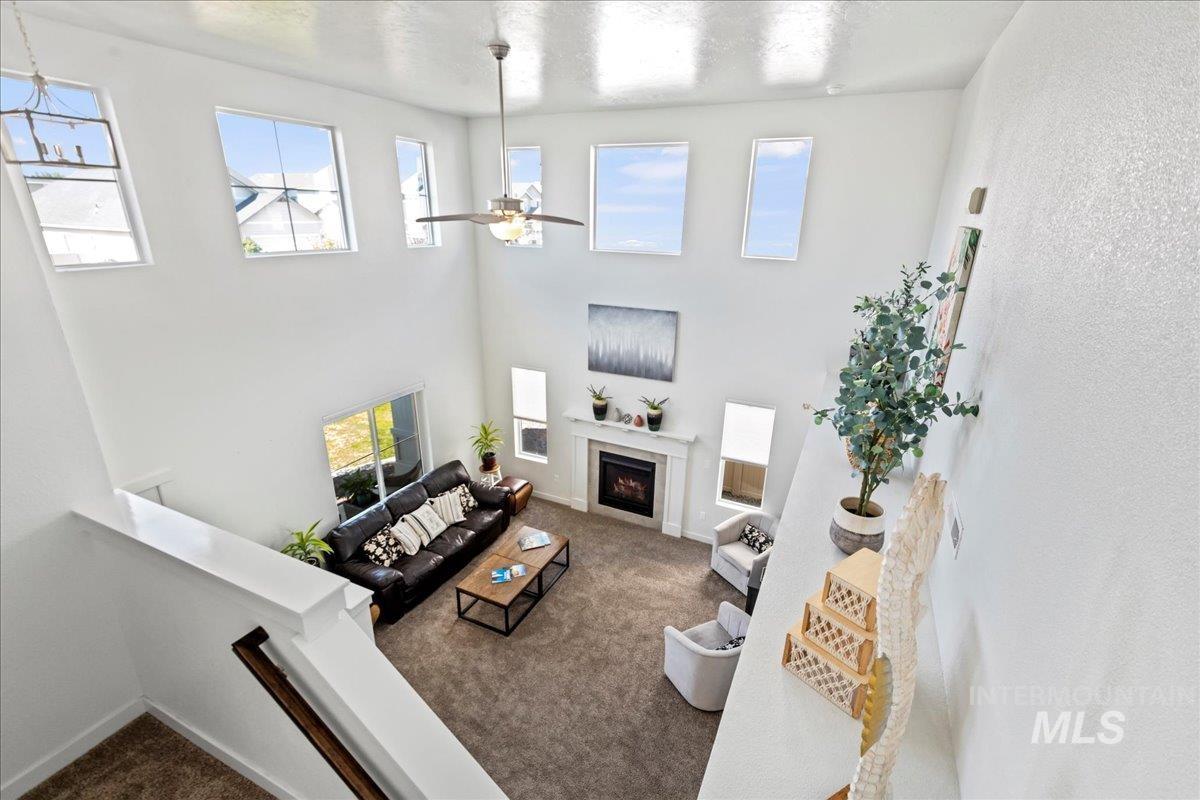 Carpeted living room with a ceiling fan, a lit fireplace, a towering ceiling, and a textured ceiling