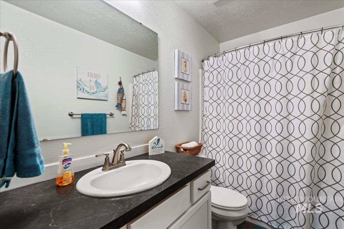 Full bath with vanity, a textured ceiling, a textured wall, and a shower with curtain