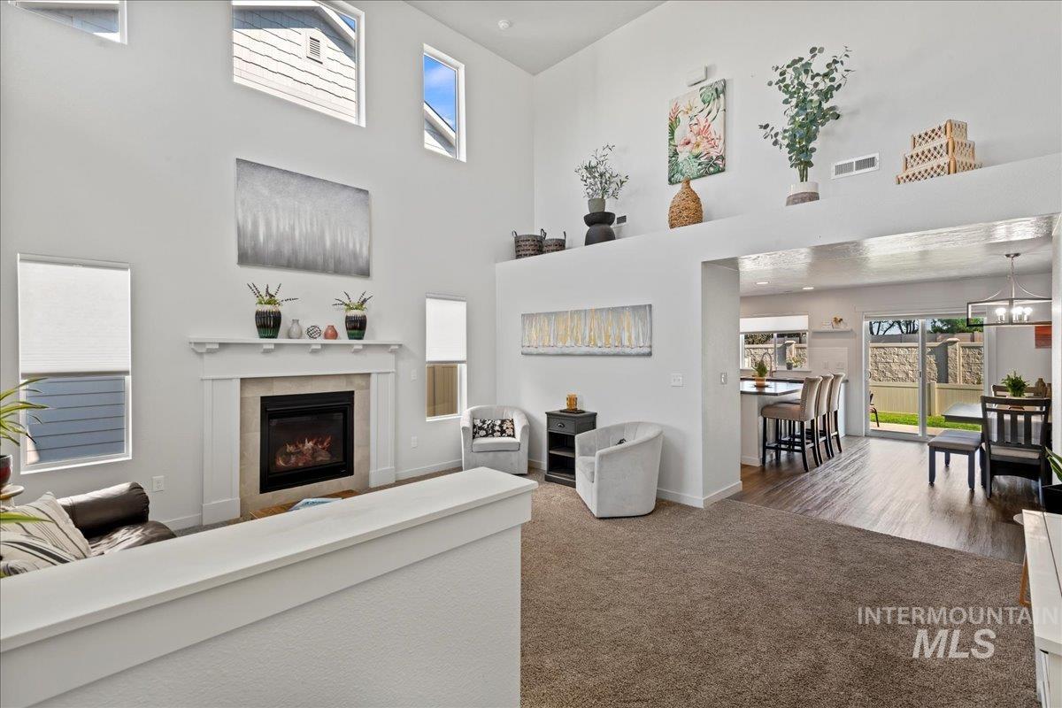 Carpeted living room with a tiled fireplace, a high ceiling, and a chandelier