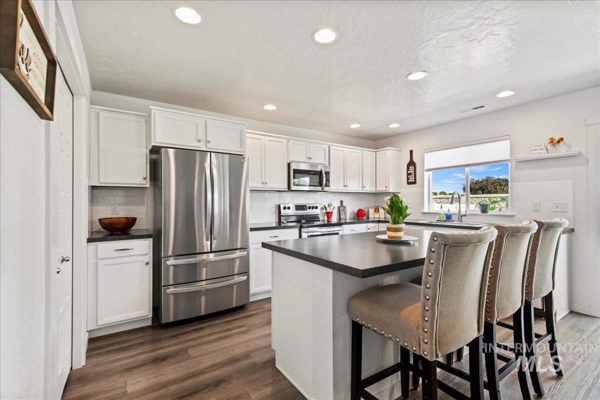 Kitchen with appliances with stainless steel finishes, dark countertops, white cabinets, recessed lighting, and a breakfast bar