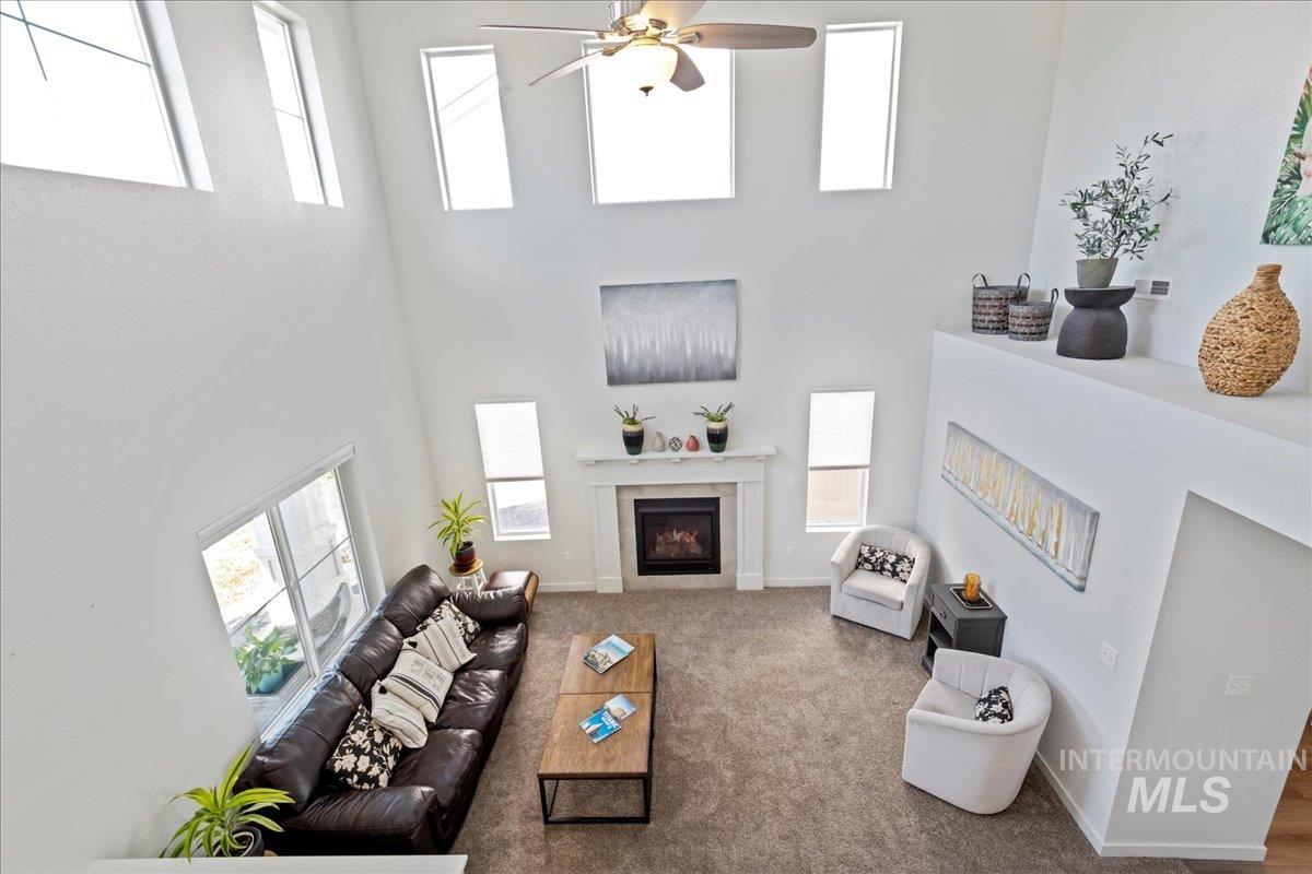 Living room featuring carpet flooring, ceiling fan, a high ceiling, and a lit fireplace