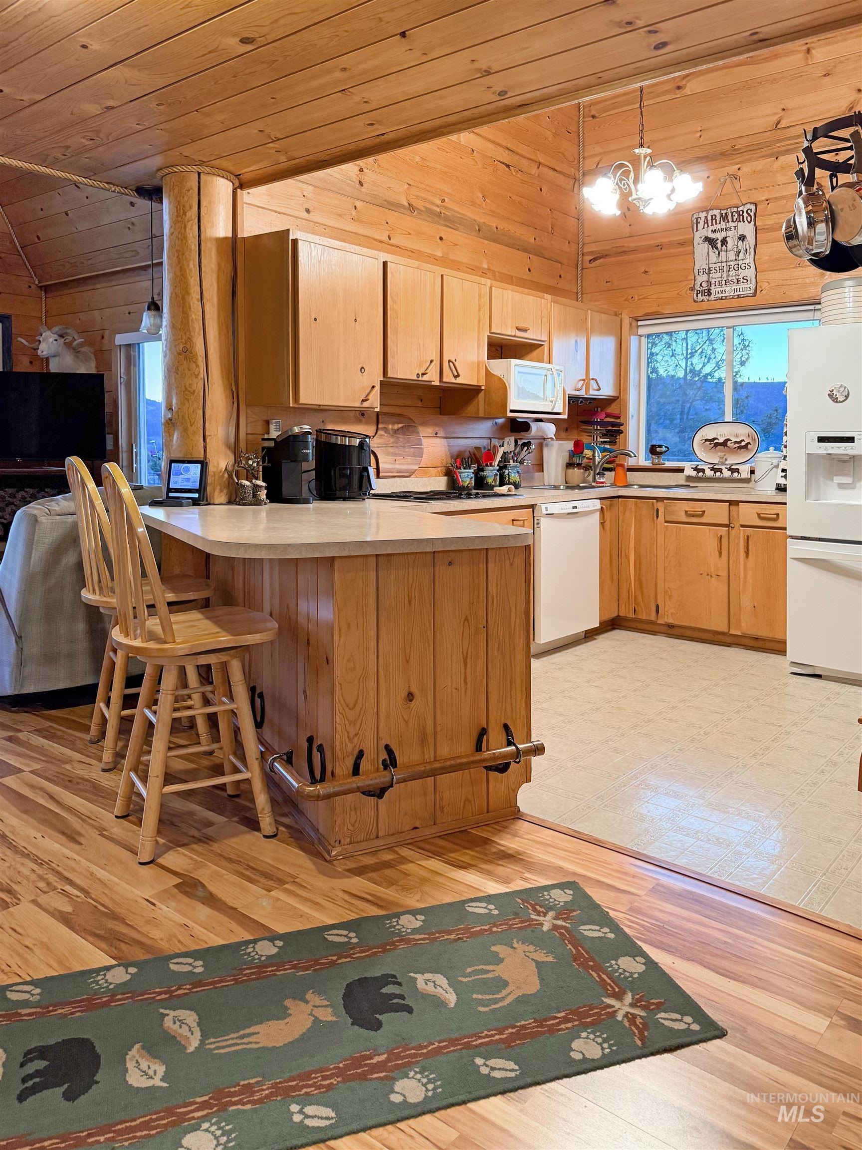 Kitchen featuring wooden ceiling, light countertops, wood walls, a breakfast bar area, and white appliances