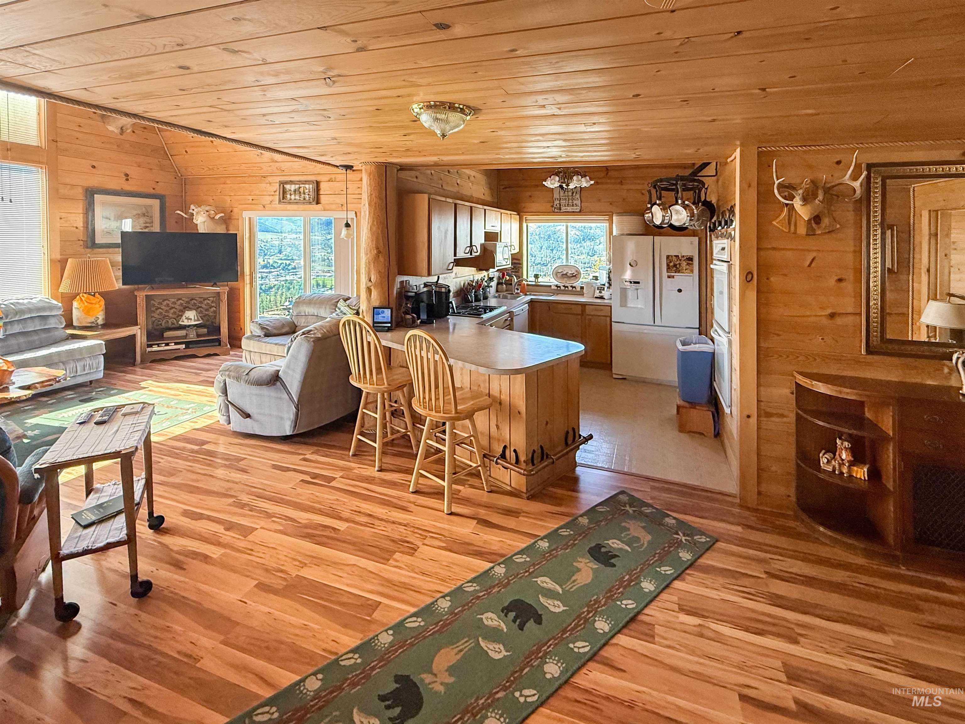 Kitchen with wood walls, wooden ceiling, a peninsula, white appliances, and vaulted ceiling