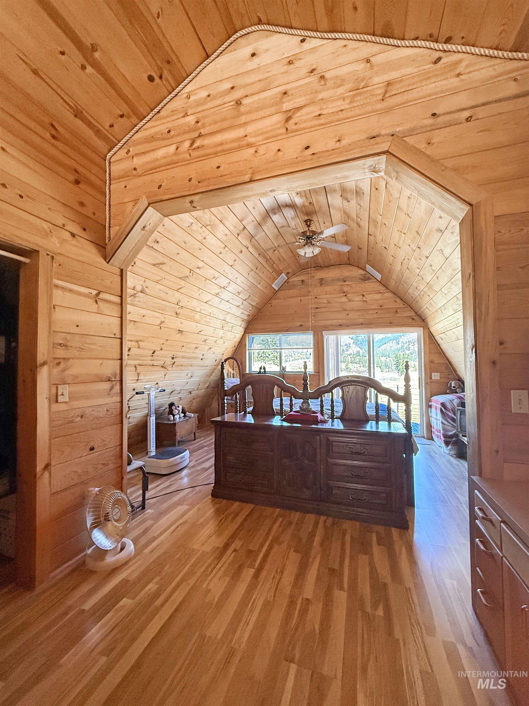Bedroom with wood ceiling, wooden walls, light wood-style floors, and vaulted ceiling