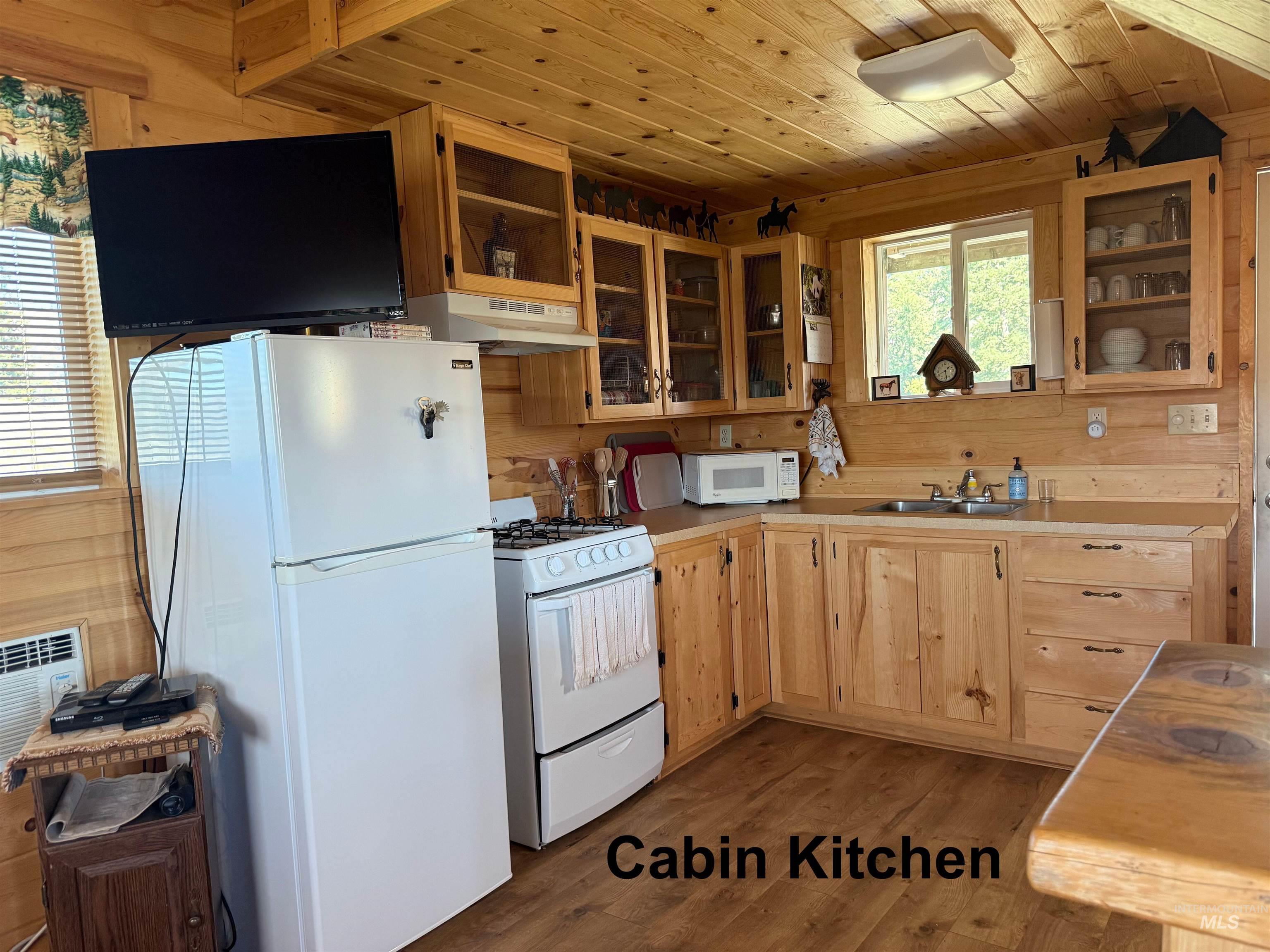 Kitchen with light wood-type flooring, white appliances, light countertops, light brown cabinetry, and wooden walls