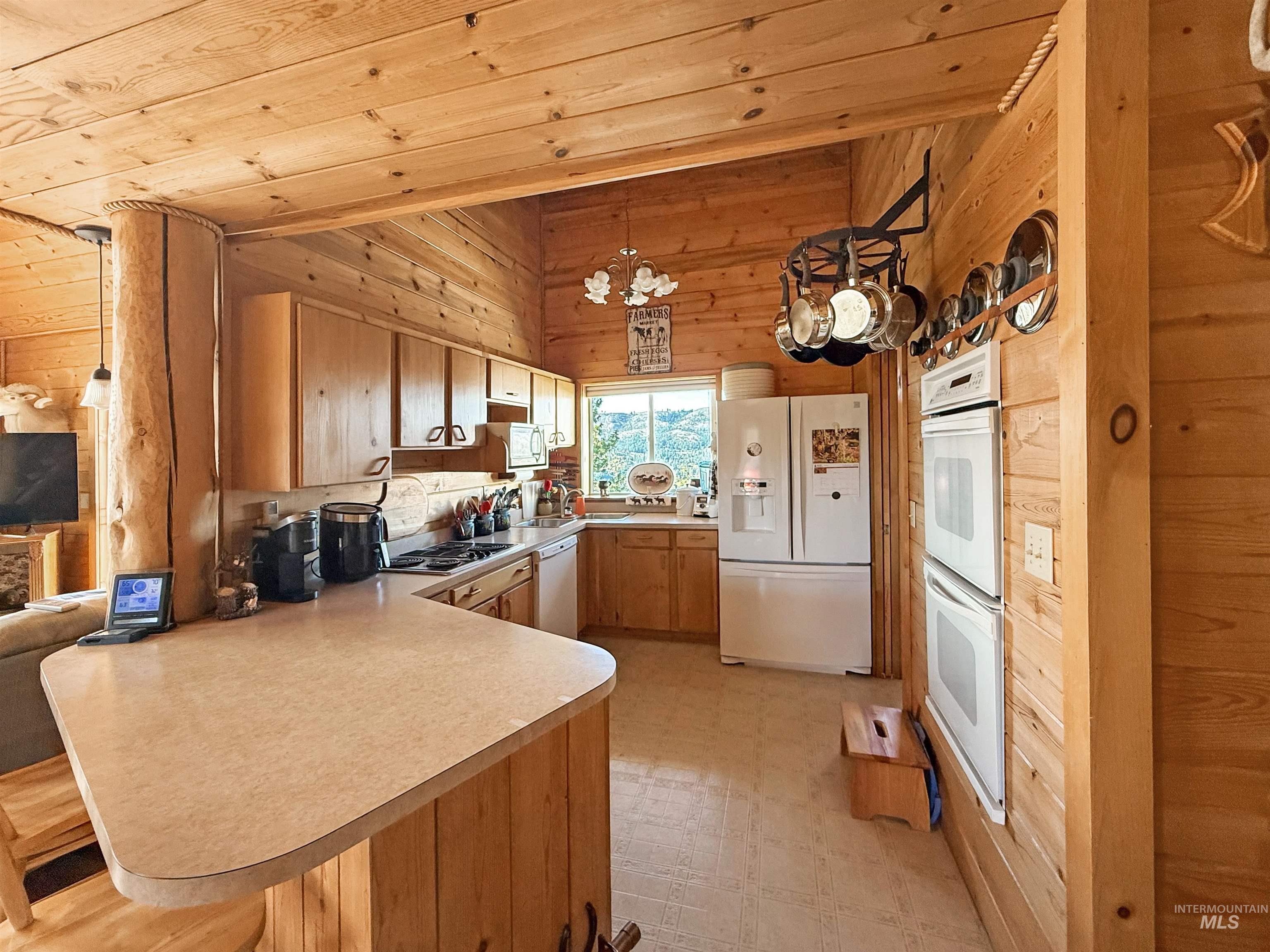 Kitchen with wood walls, light flooring, white appliances, a peninsula, and light countertops