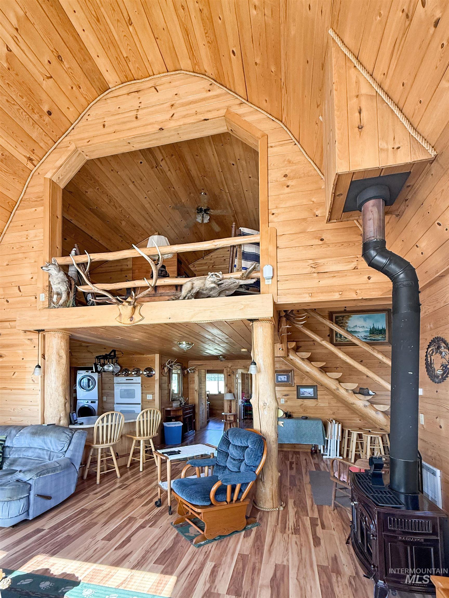 Living area with wood walls, a wood stove, wood ceiling, stairs, and light wood-style floors