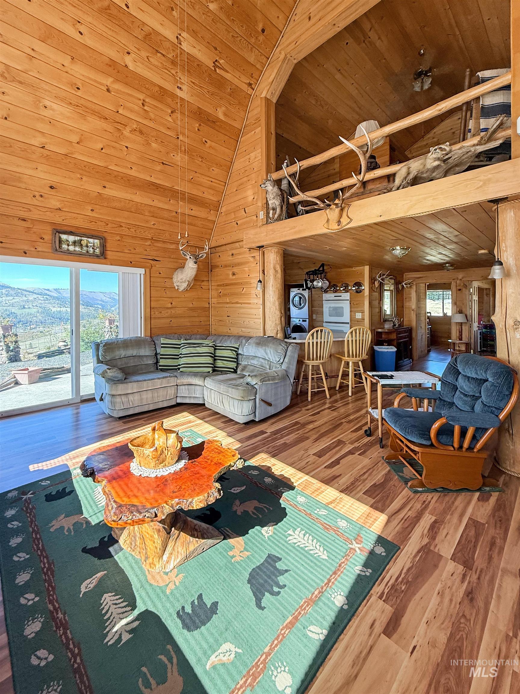 Living area with wood finished floors, wood walls, high vaulted ceiling, wooden ceiling, and washer / clothes dryer