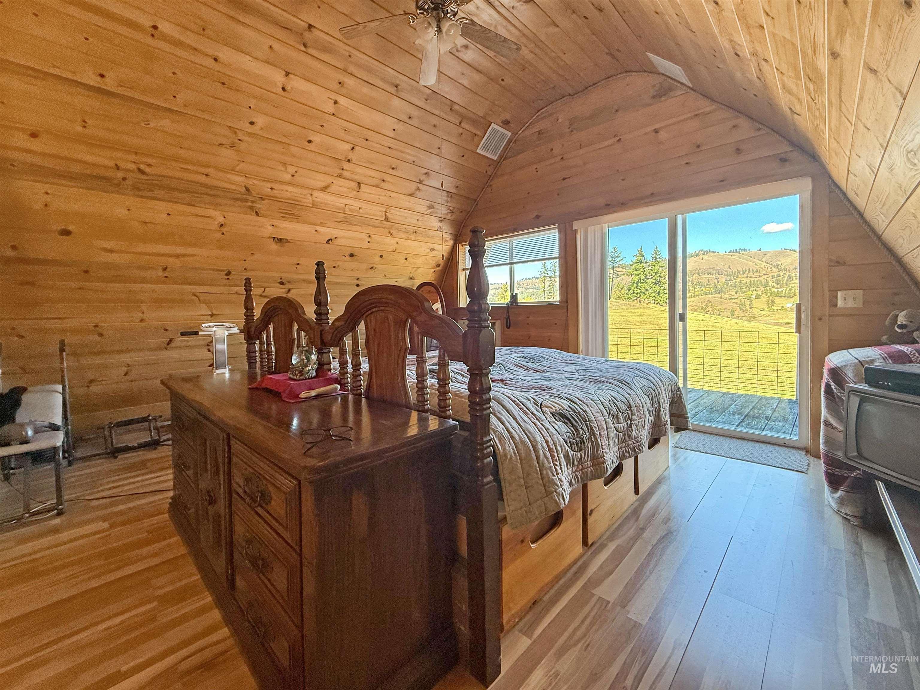 Bedroom with wooden walls, light wood finished floors, wood ceiling, vaulted ceiling, and access to exterior