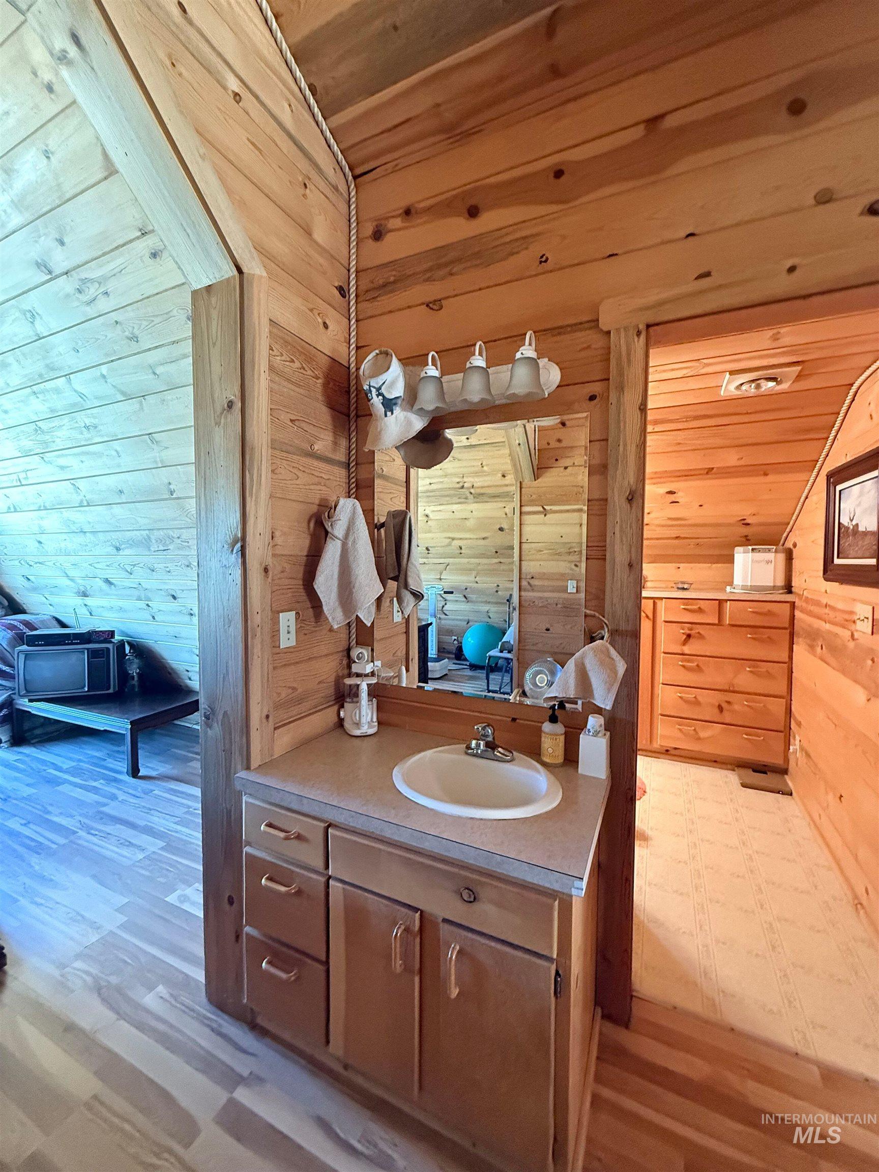Bathroom with vanity, wooden walls, wood ceiling, and light wood-type flooring
