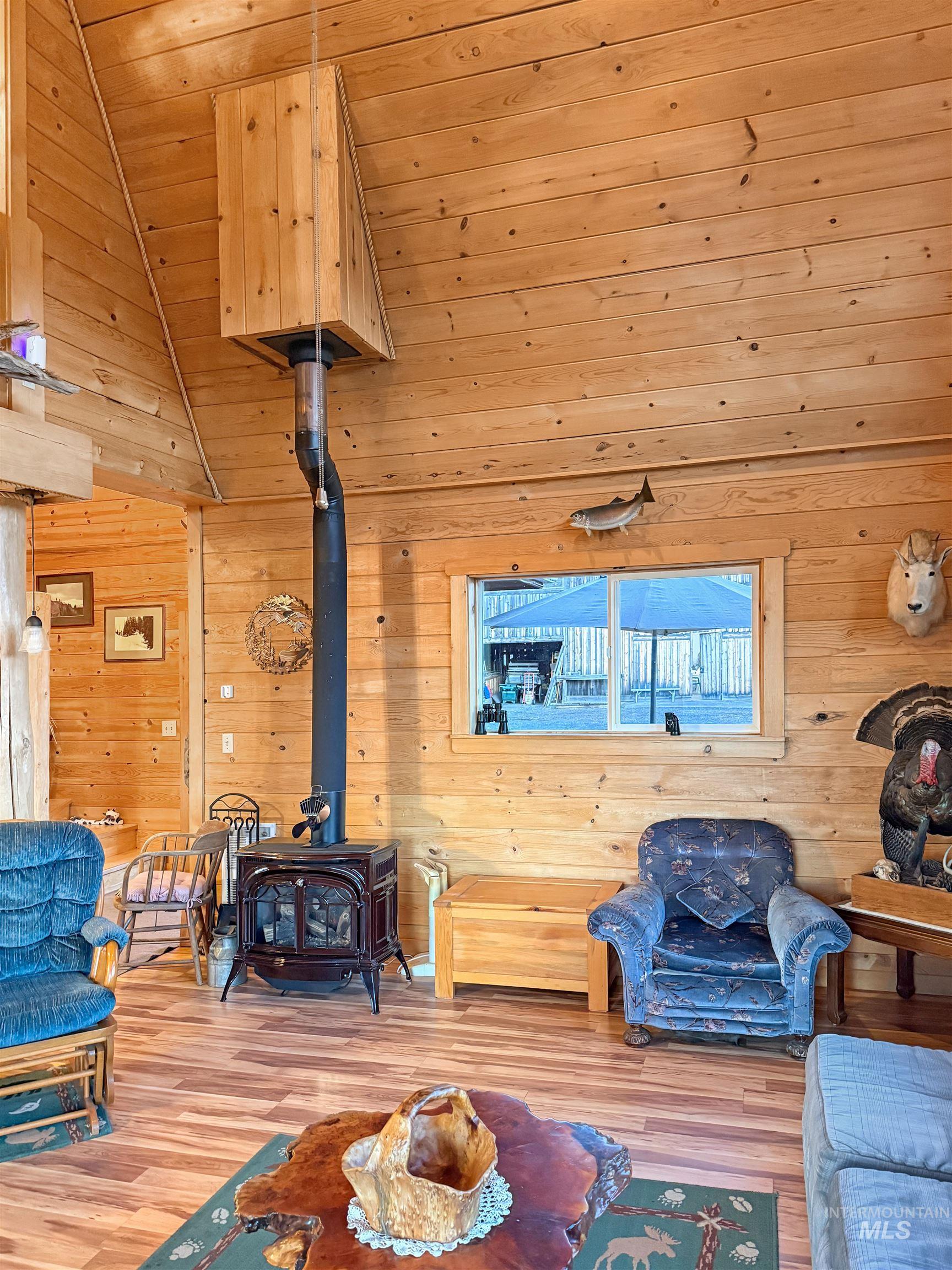 Living room with a wood stove, wooden ceiling, wood finished floors, wooden walls, and vaulted ceiling