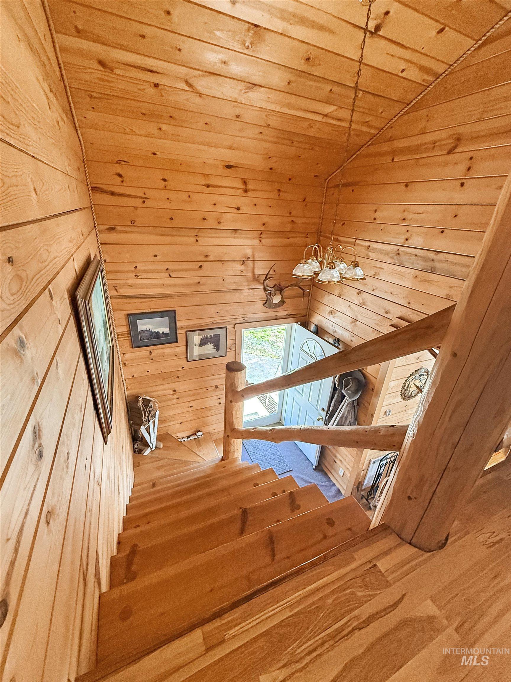 Stairway featuring wooden walls, wood ceiling, high vaulted ceiling, wood-type flooring, and a chandelier