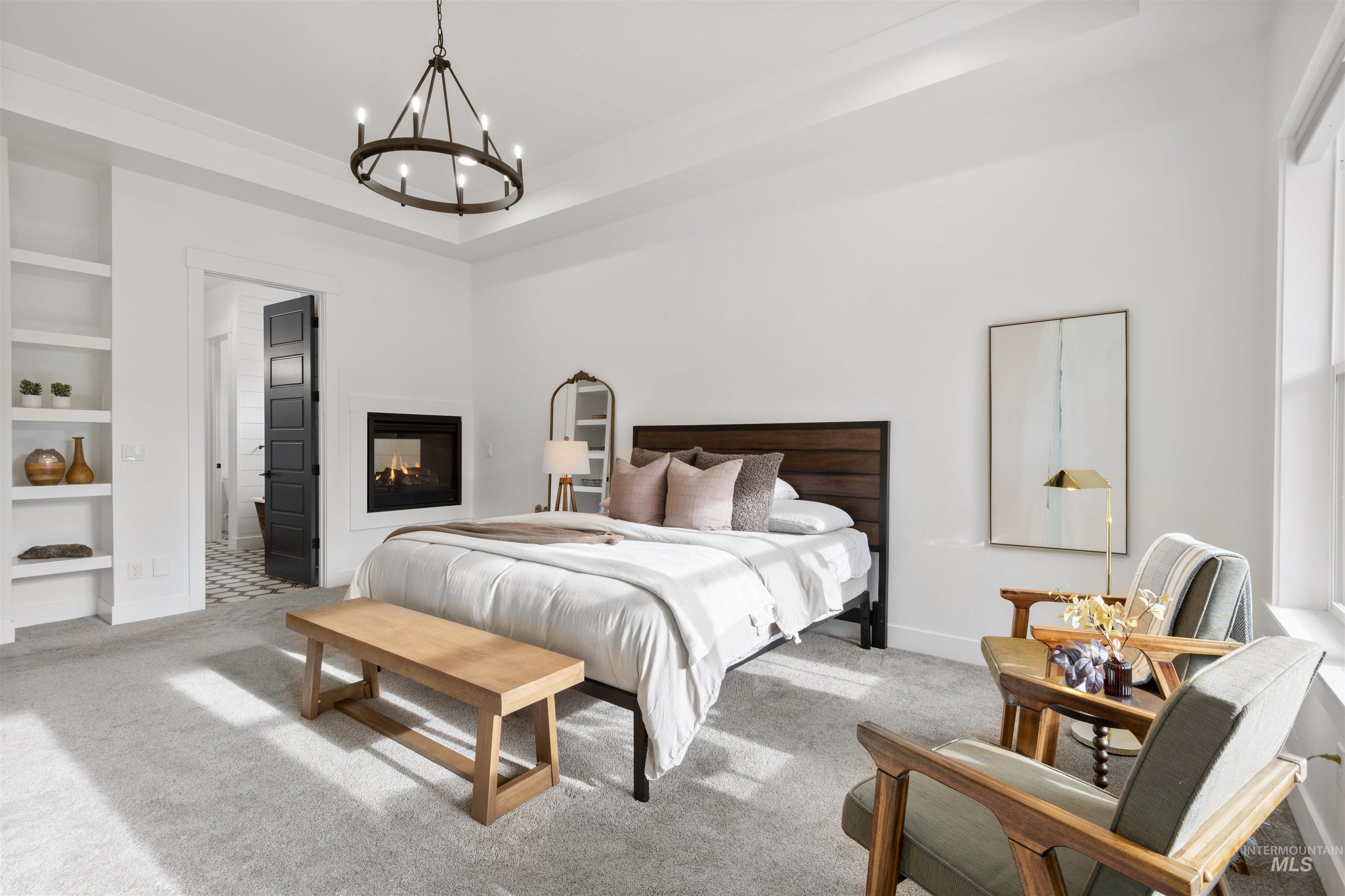 Carpeted bedroom with a chandelier, a tray ceiling, and a multi sided fireplace