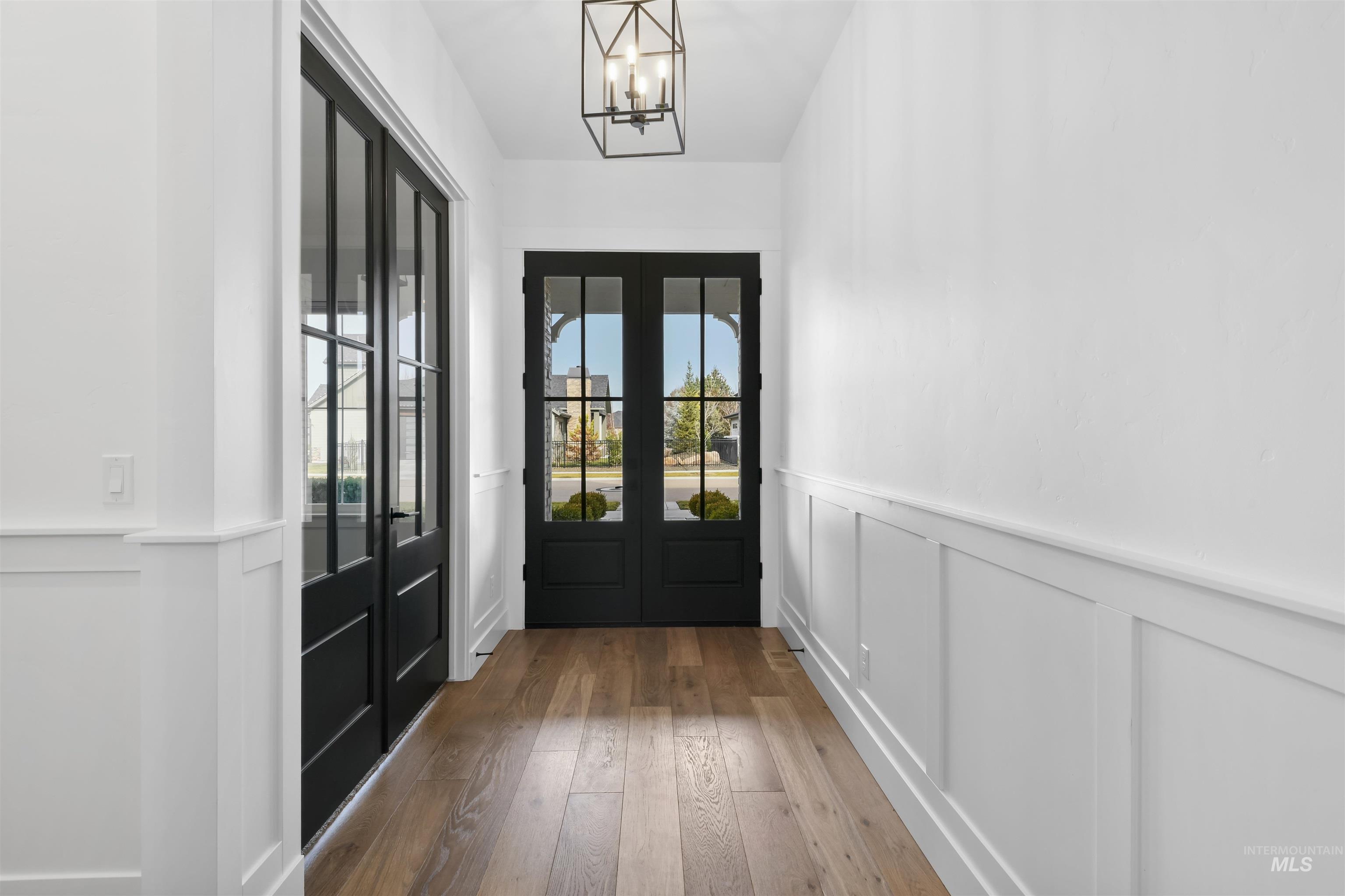 Doorway to outside featuring a wainscoted wall, a decorative wall, wood-type flooring, a chandelier, and french doors
