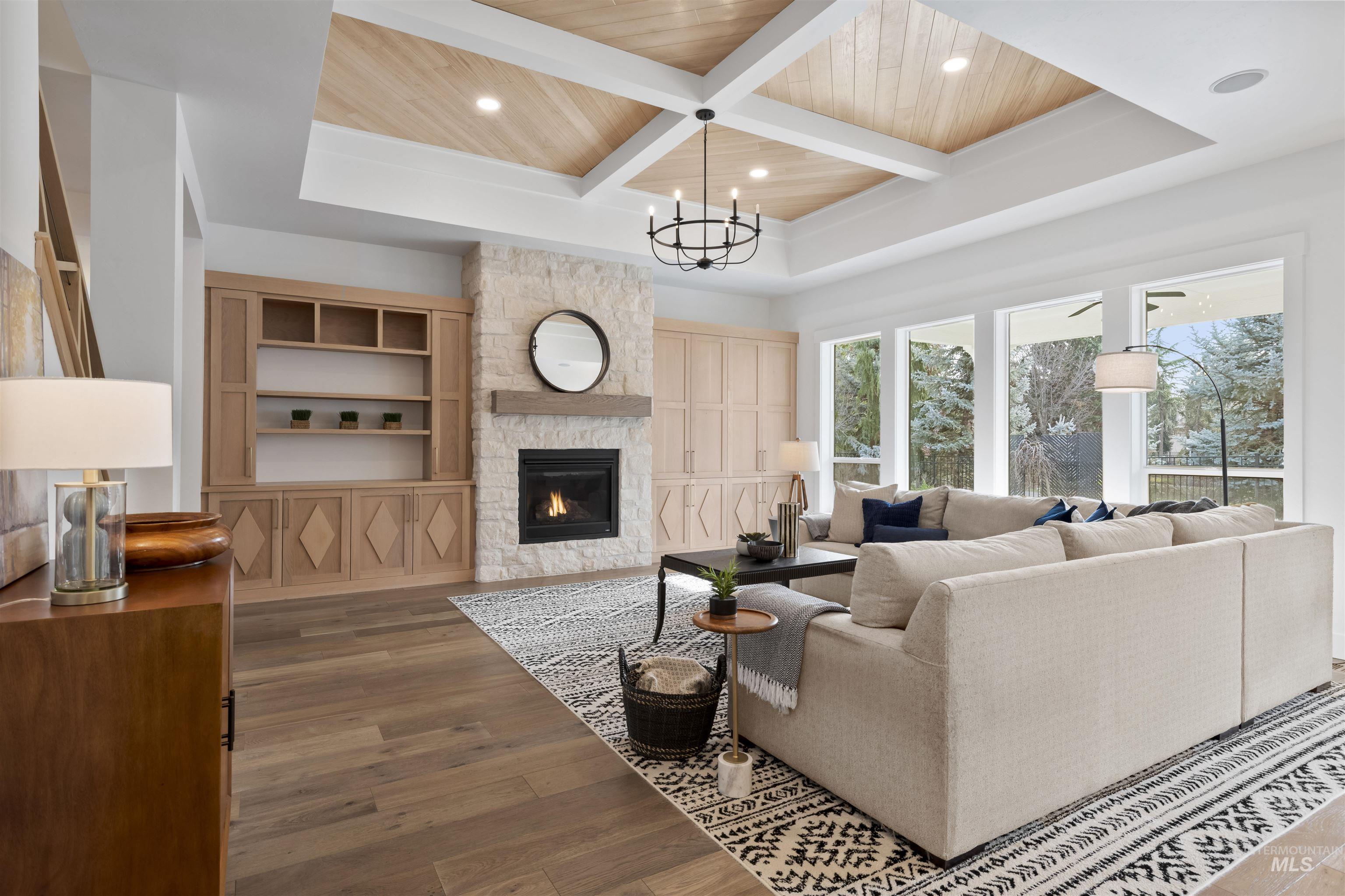 Living area with a wooden ceiling with exposed beams, dark wood-style floors, a stone fireplace, coffered ceiling, and a chandelier