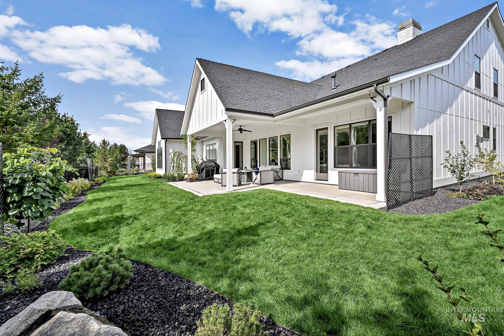Back of property featuring a ceiling fan, a shingled roof, board and batten siding, a patio, and a chimney