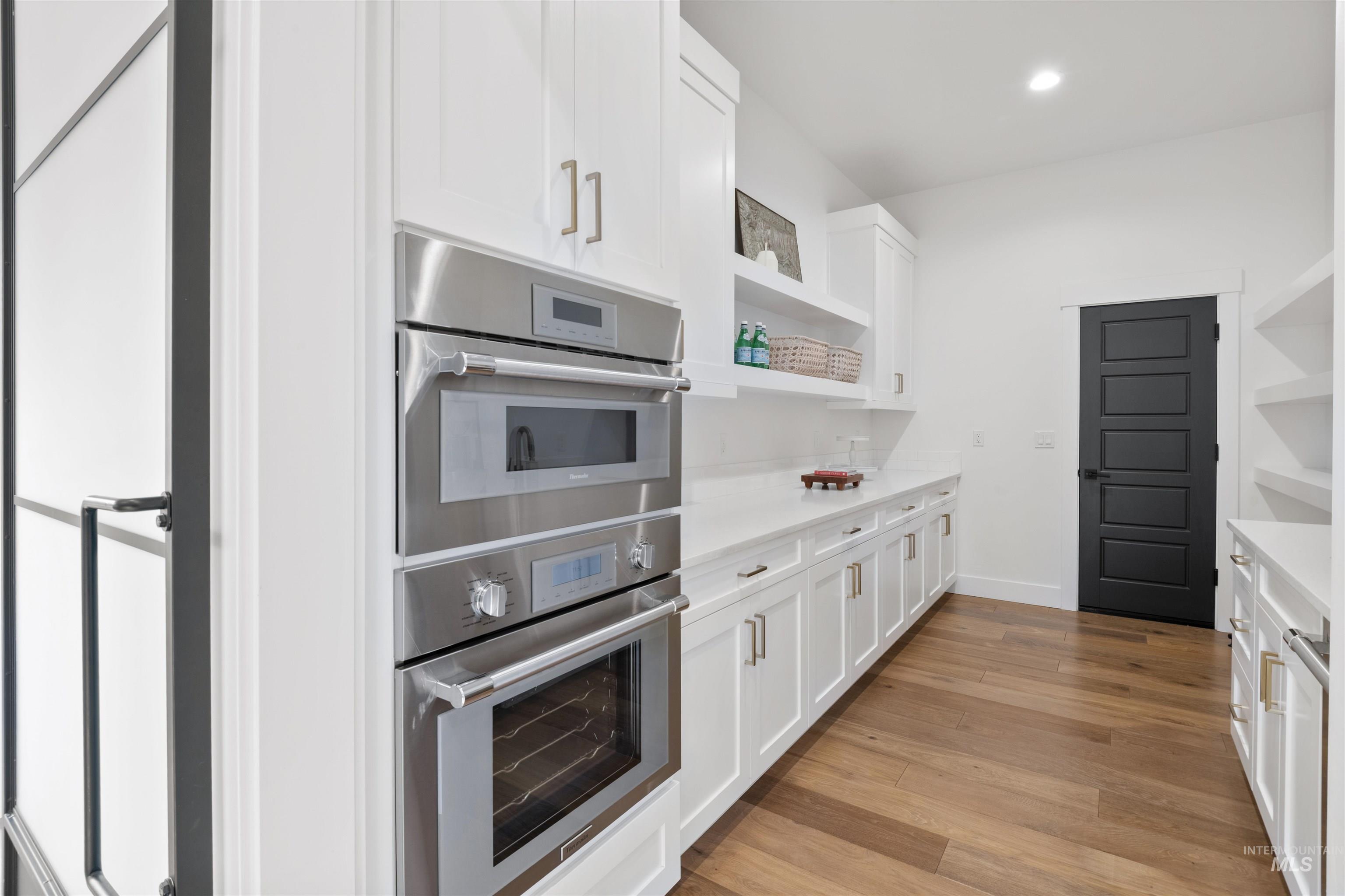 Kitchen with open shelves, stainless steel double oven, white cabinetry, and recessed lighting