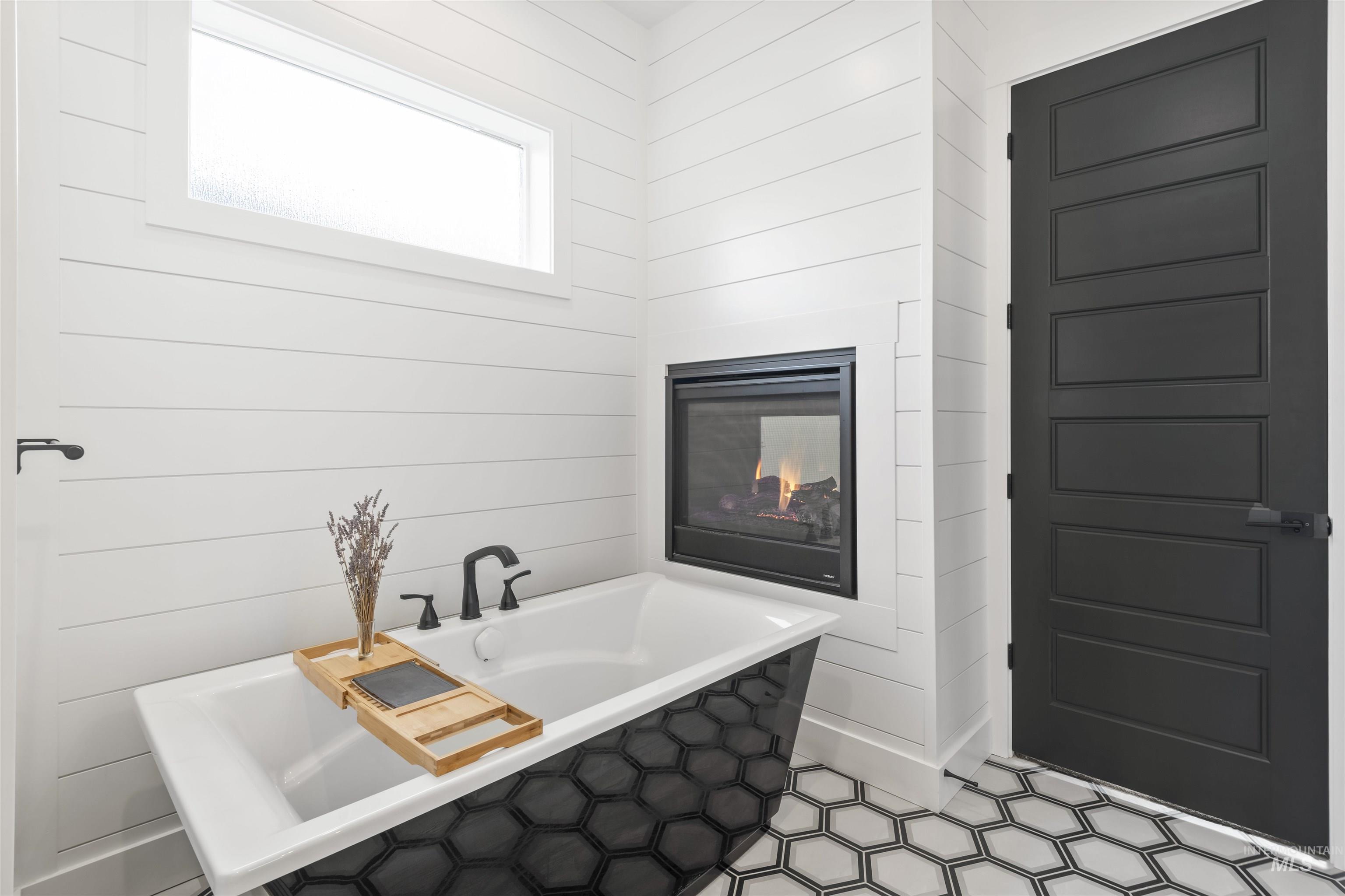 Bathroom with a soaking tub, a glass covered fireplace, and wooden walls