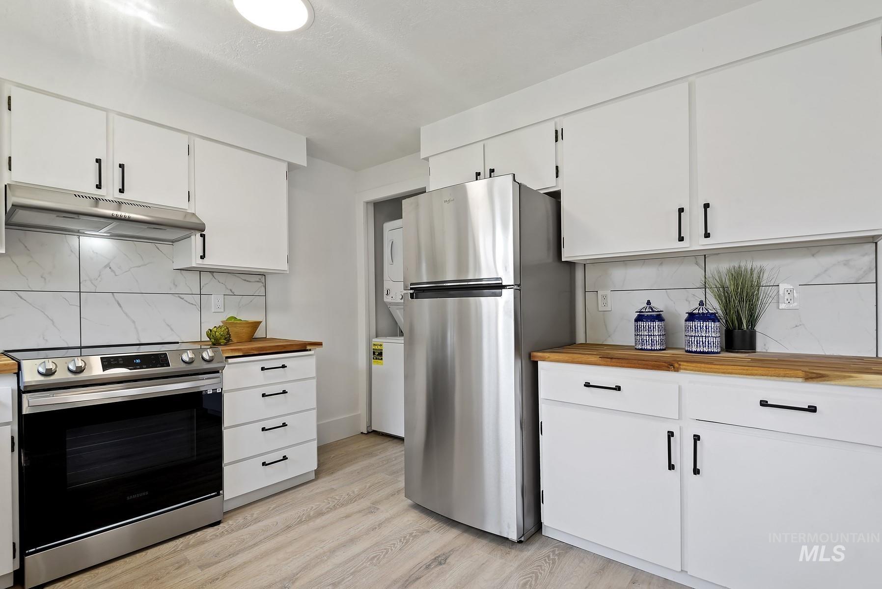 Kitchen featuring decorative backsplash, stainless steel appliances, under cabinet range hood, and white cabinetry