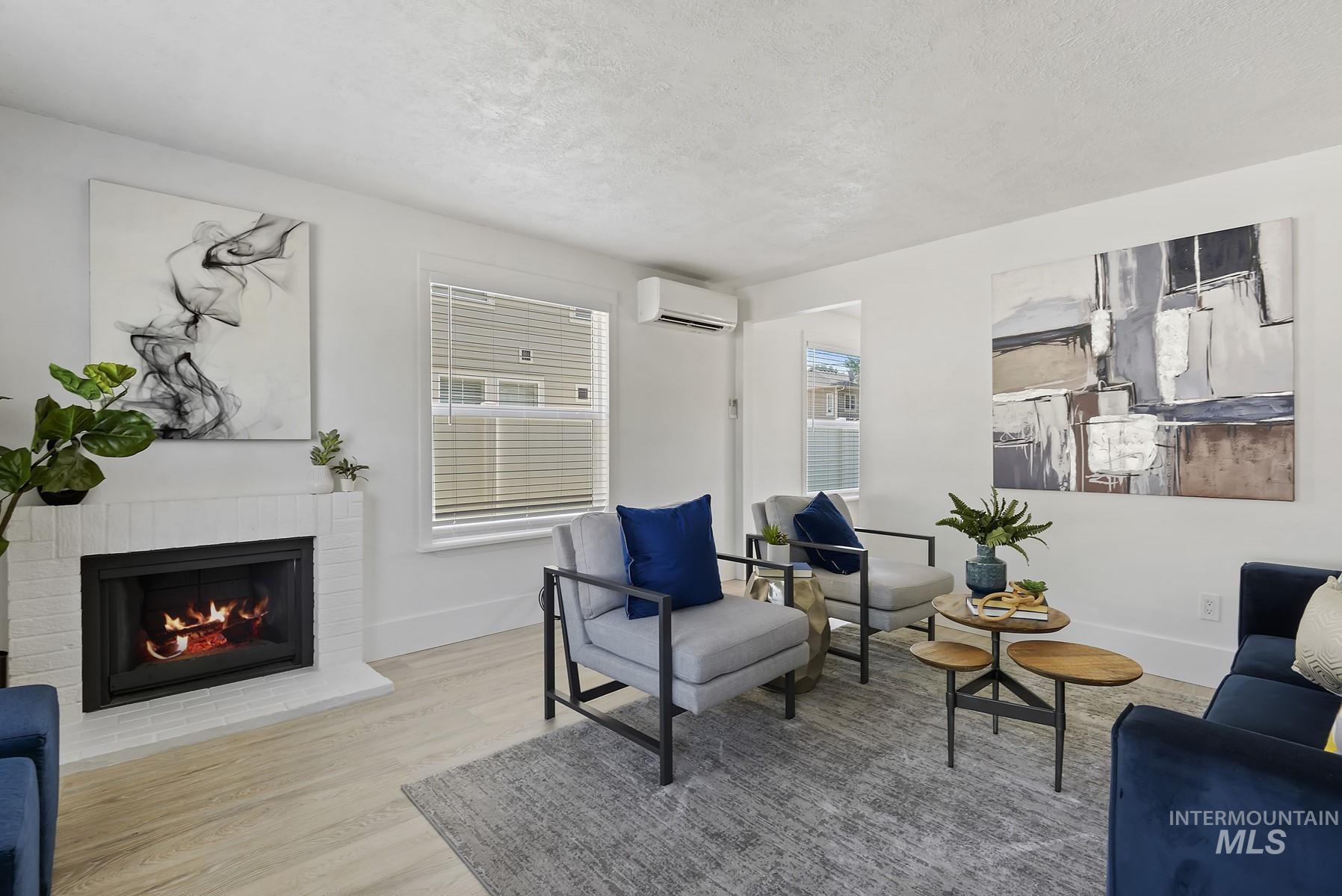 Living area with a textured ceiling, healthy amount of natural light, wood finished floors, a brick fireplace, and a wall unit AC