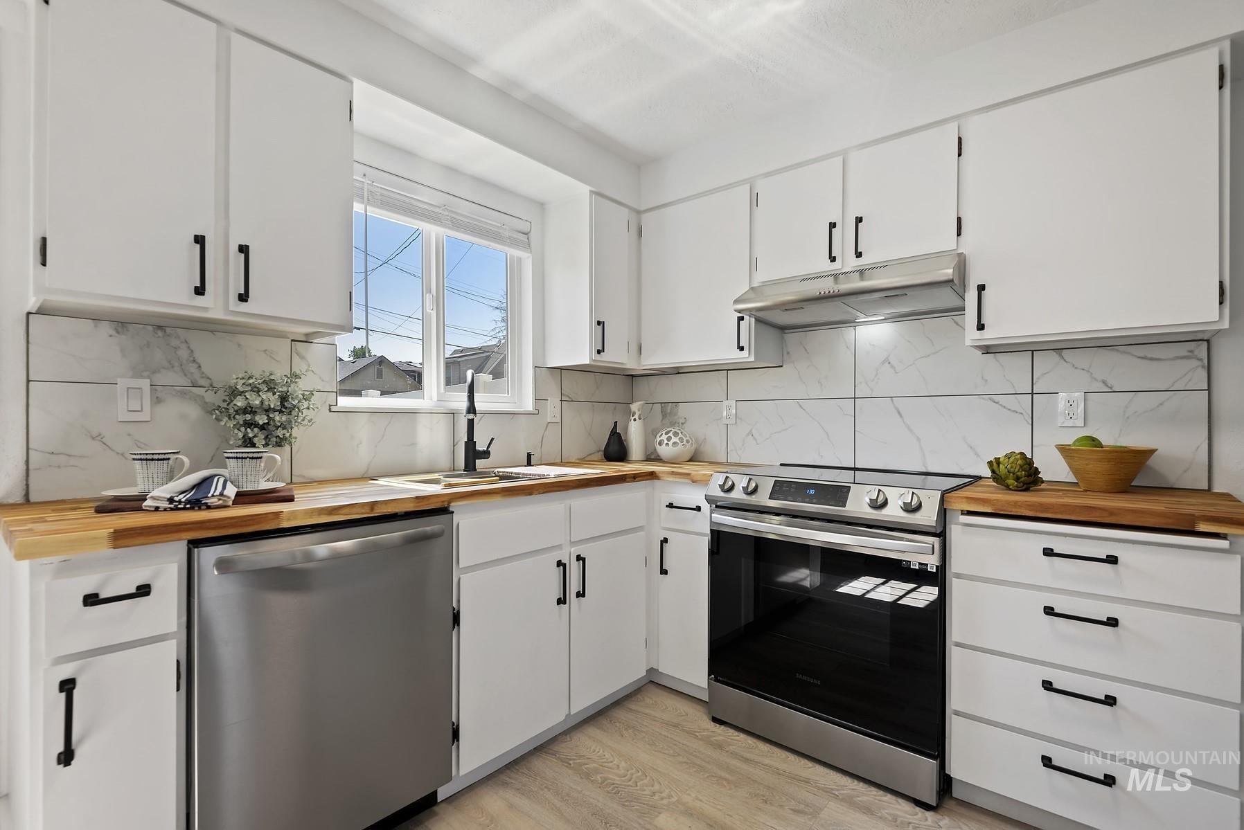 Kitchen with appliances with stainless steel finishes, white cabinets, light wood-type flooring, under cabinet range hood, and butcher block countertops