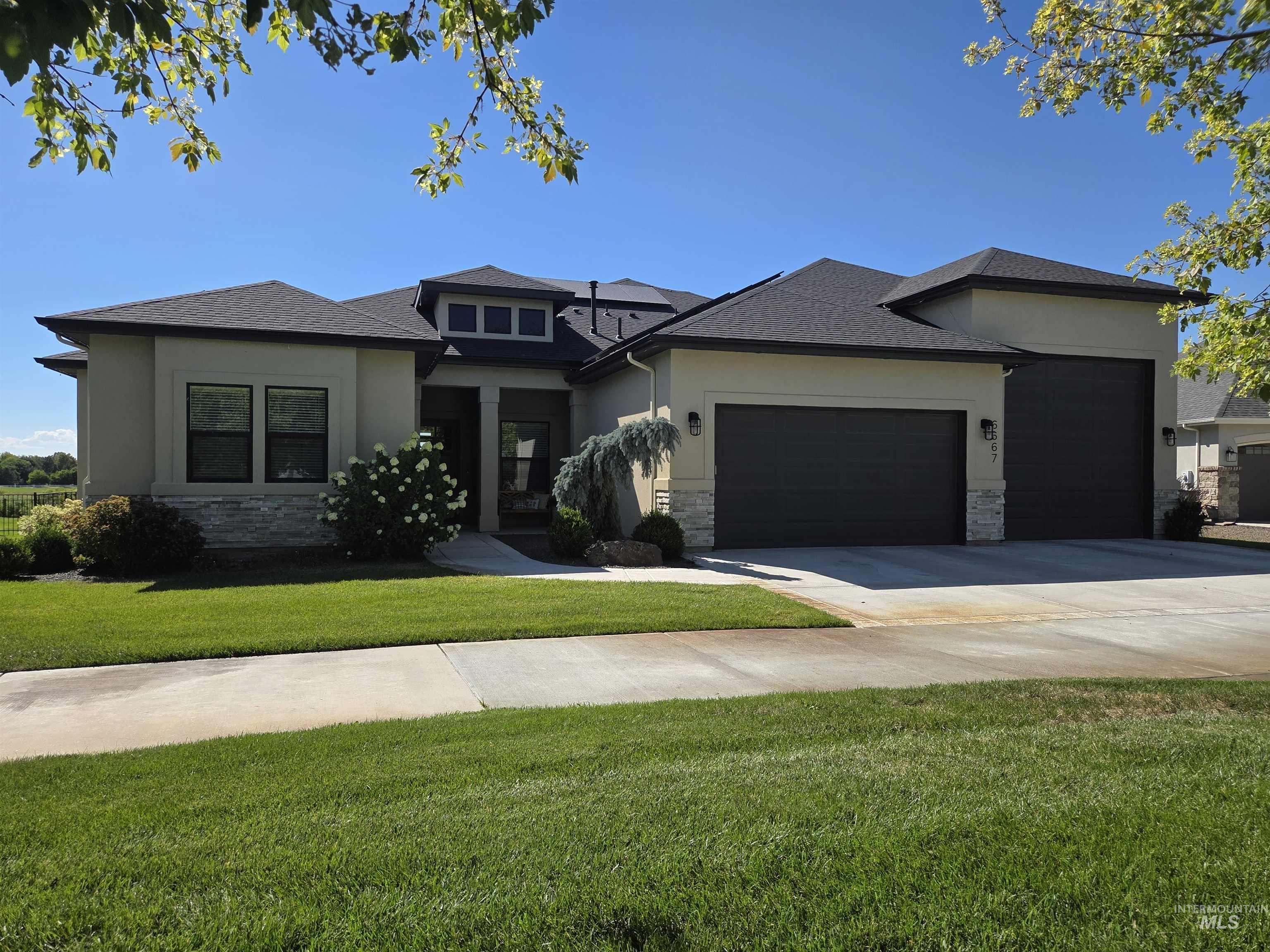 Prairie-style house with an attached garage, stone siding, a front lawn, and stucco siding