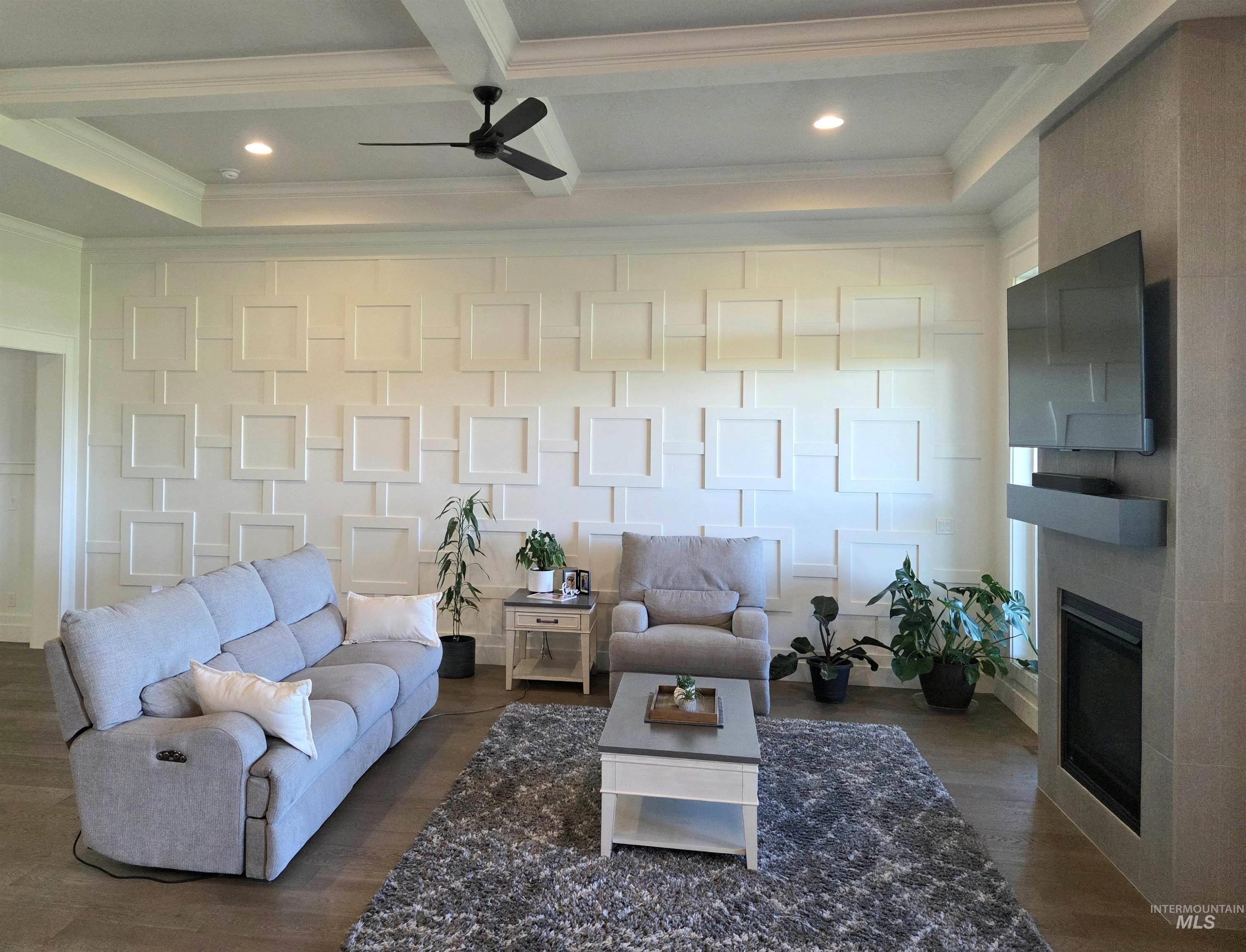 Living area with recessed lighting, a glass covered fireplace, ornamental molding, dark wood finished floors, and beam ceiling
